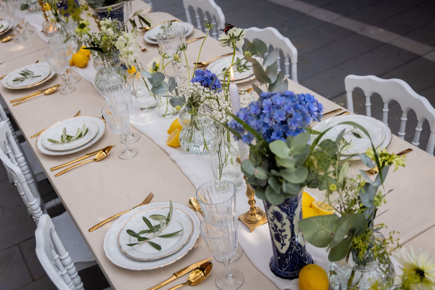 An elegant wedding table setting with blue hydrangeas, delicate wildflowers, and yellow accents on a white tablecloth.