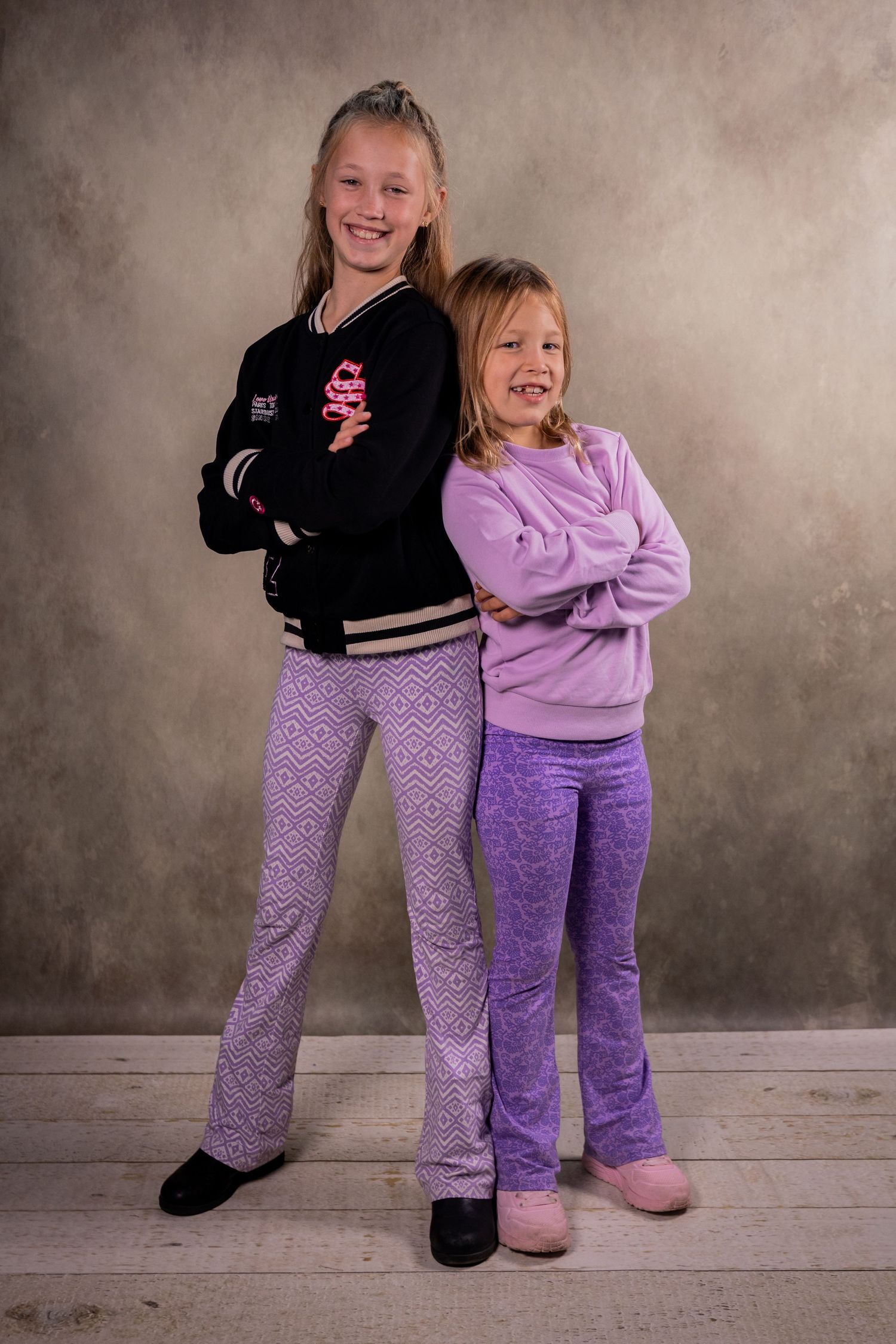 Two children in matching purple pants and contrasting tops posing against a studio backdrop.