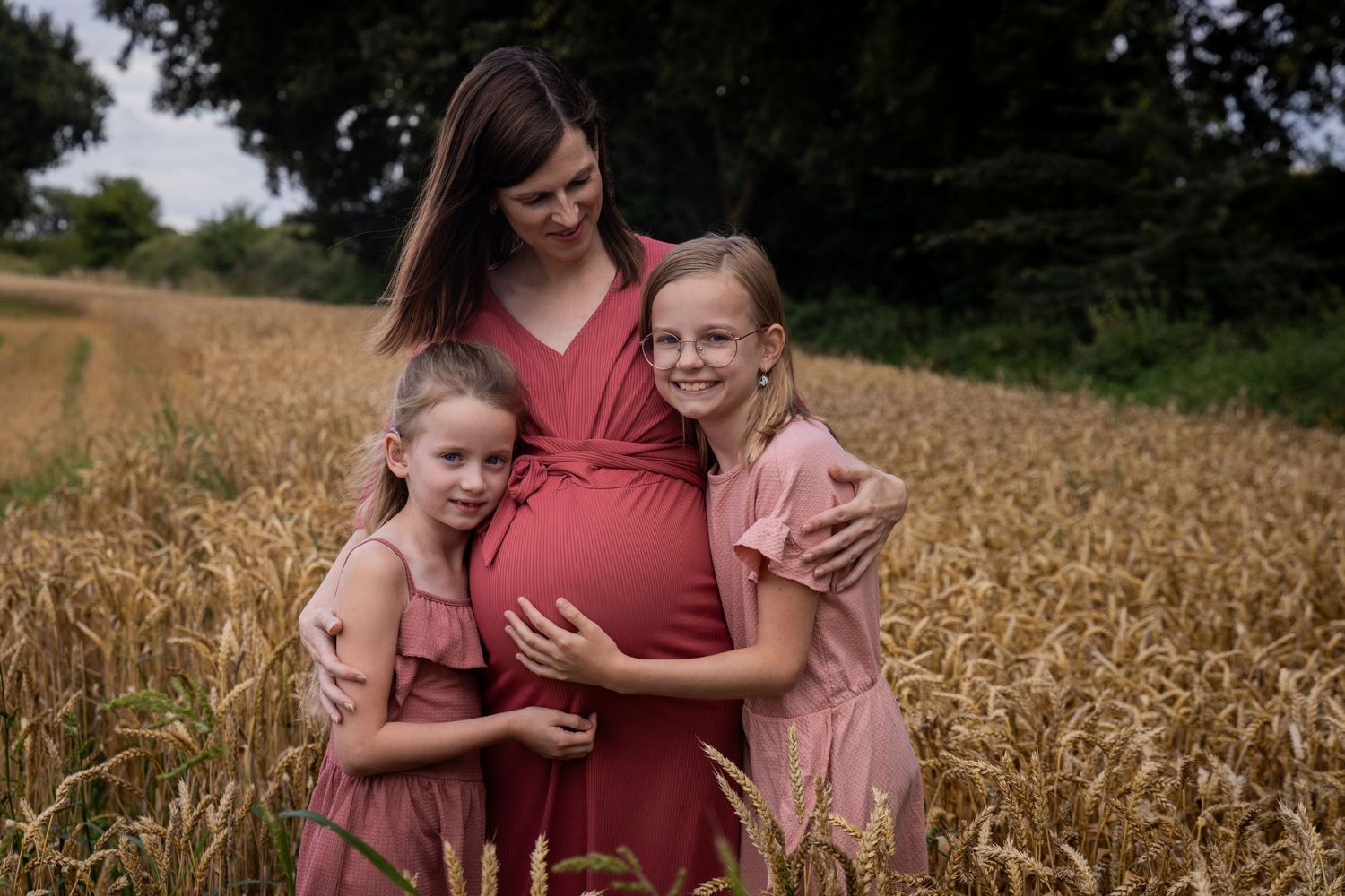 A maternity photoshoot in a golden wheat field with children embracing the moment.