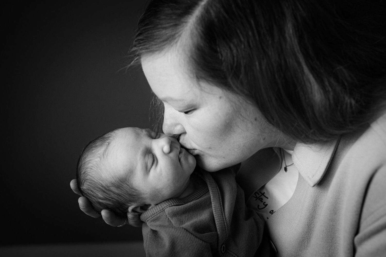 Tender black and white moment between parent and newborn in soft lighting.