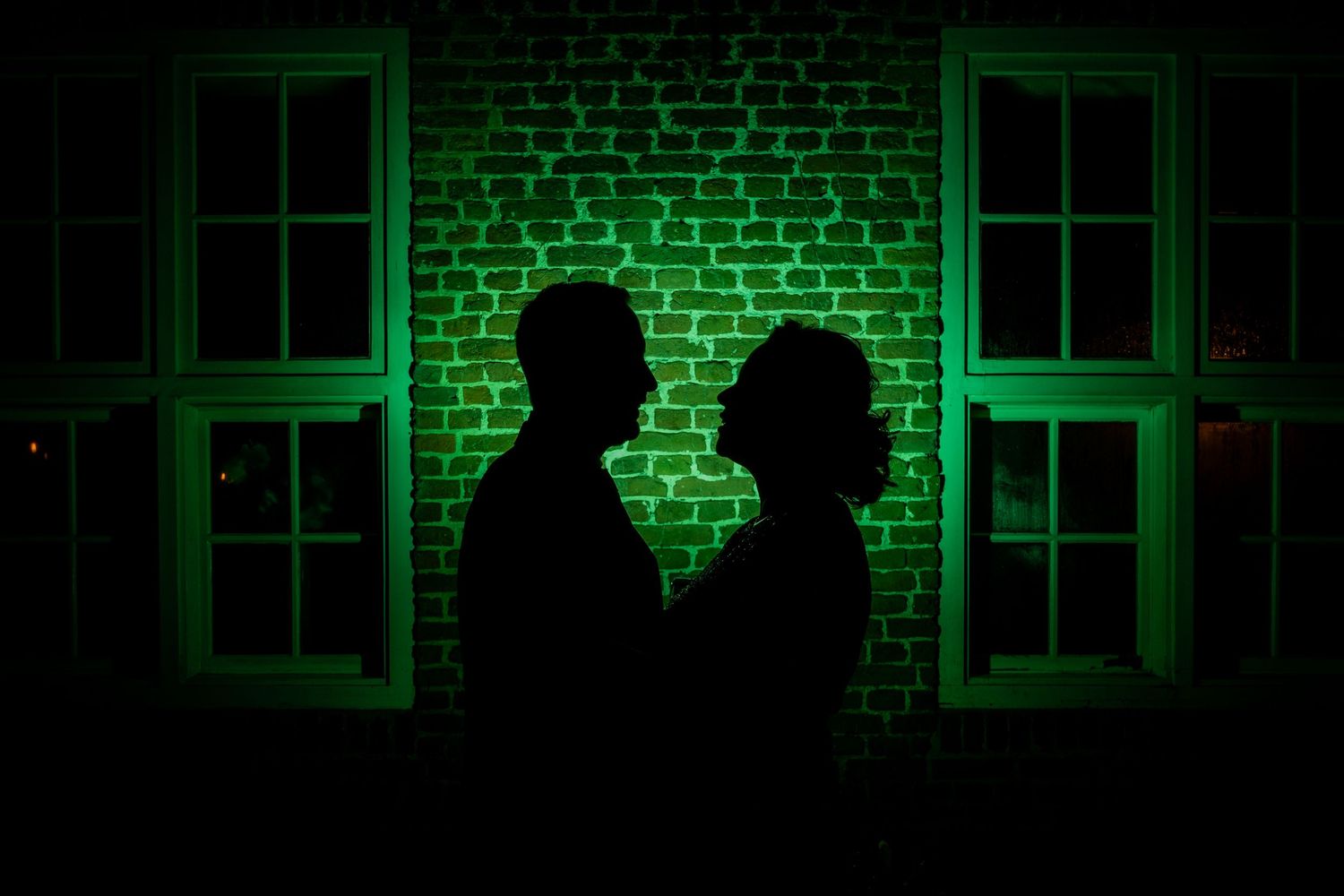 Atmospheric green-lit silhouettes create dramatic wedding reception moments against brick walls.