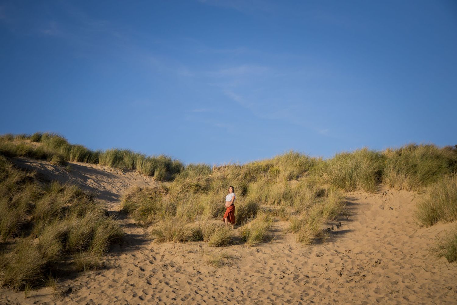 Distant figure climbing sandy path through beach dunes under blue sky.
