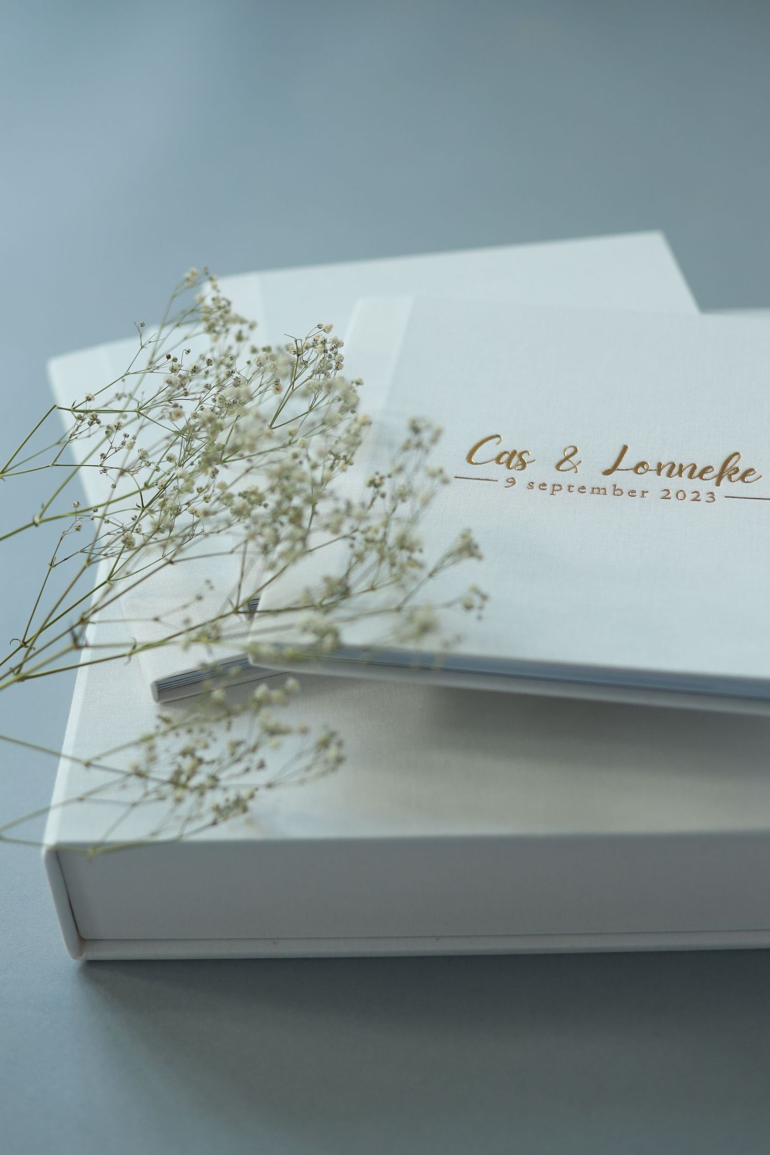 A minimalist white wedding album with gold text and delicate baby's breath flowers resting on top of it.