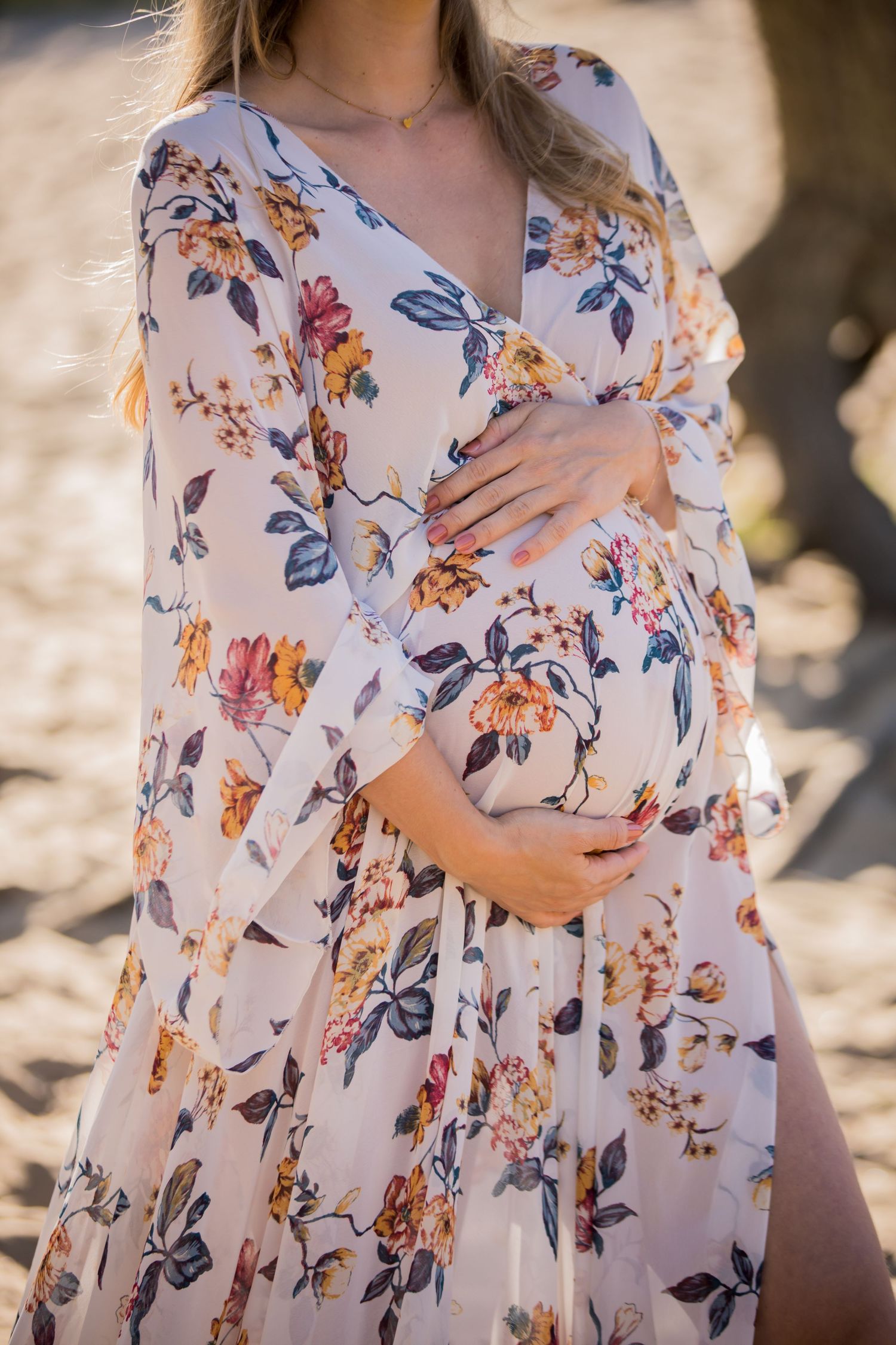 Close-up of floral maternity dress with hands cradling baby bump.