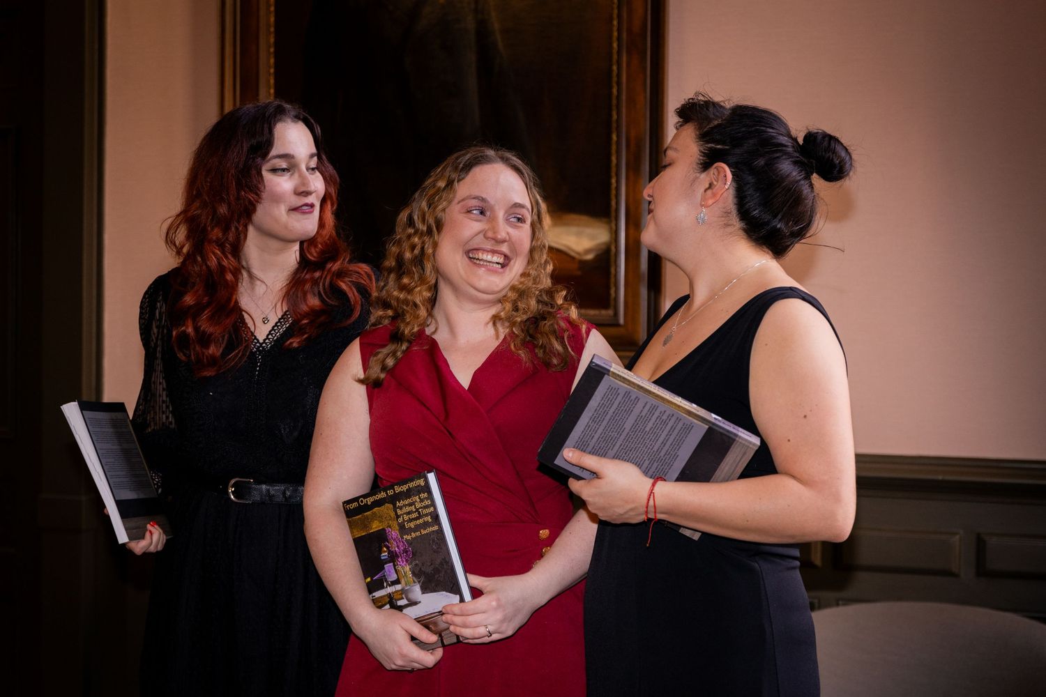Women laughing together while sharing books in an indoor gathering.