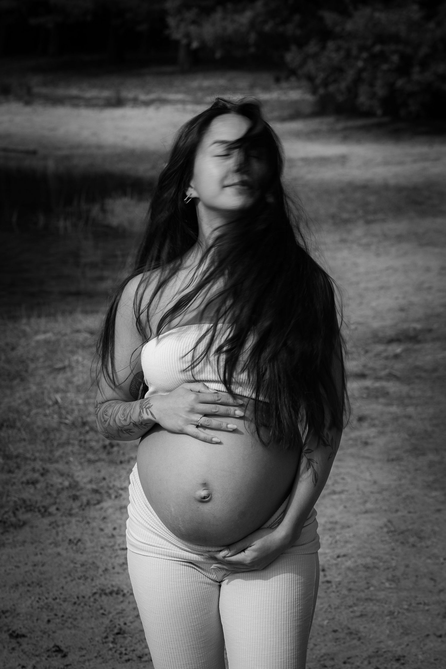 Black and white maternity portrait with serene expression and hands cradling bump.