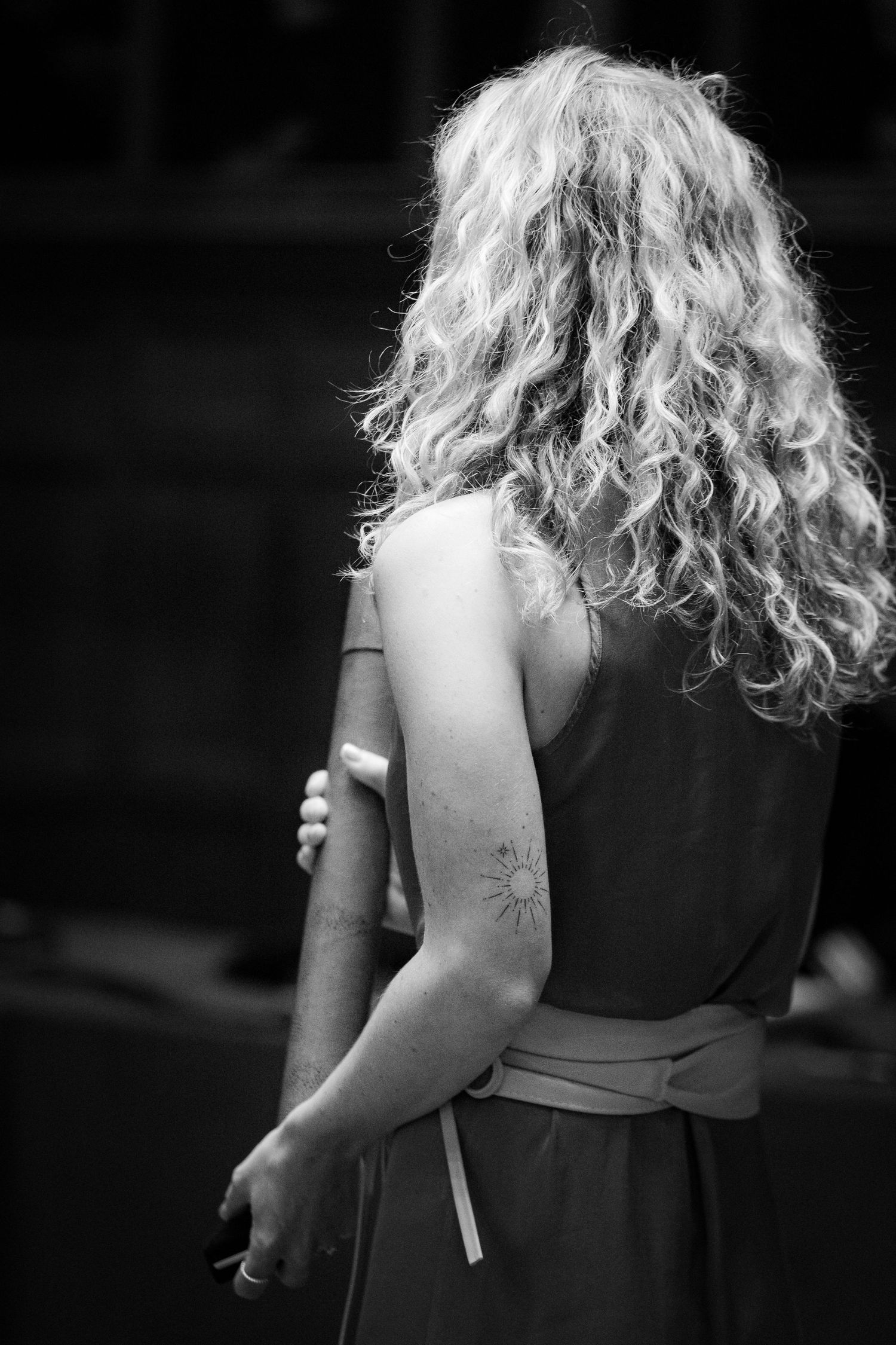 Black and white rear view of person with curly hair in formal dress.