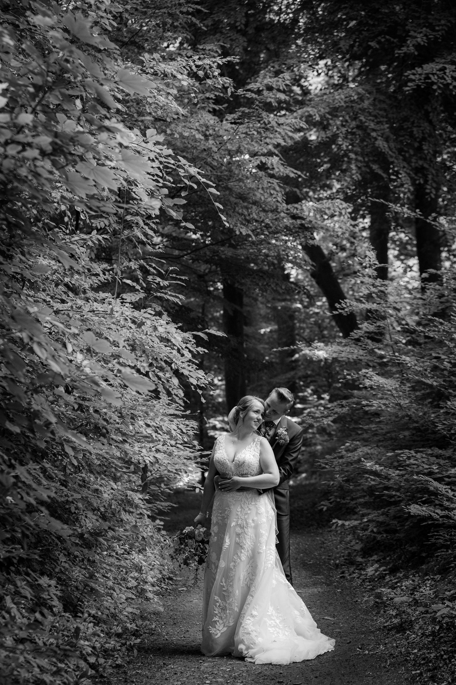 Black and white portrait of bride standing on wooded path surrounded by dramatic forest scenery.