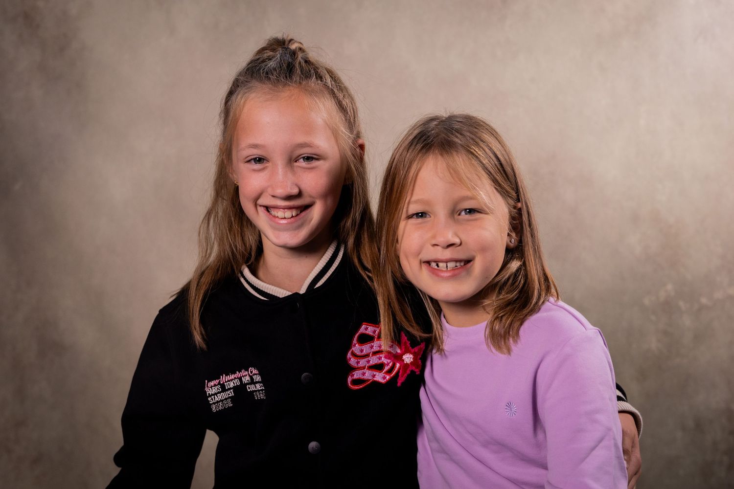 Studio portrait of two siblings wearing black and purple outfits against a neutral background.