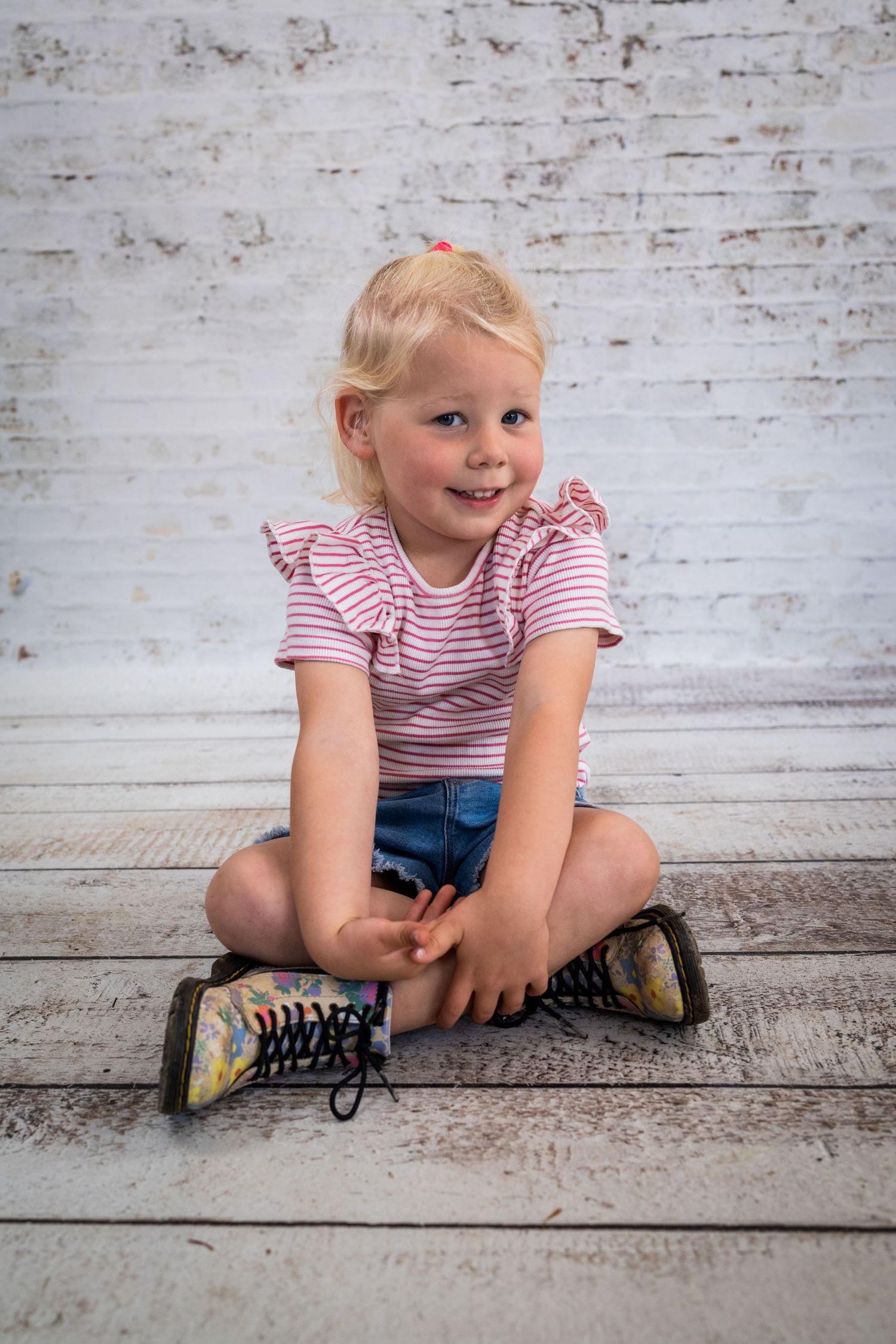 Child in pink striped shirt sitting on wooden floor showing playful expressions.