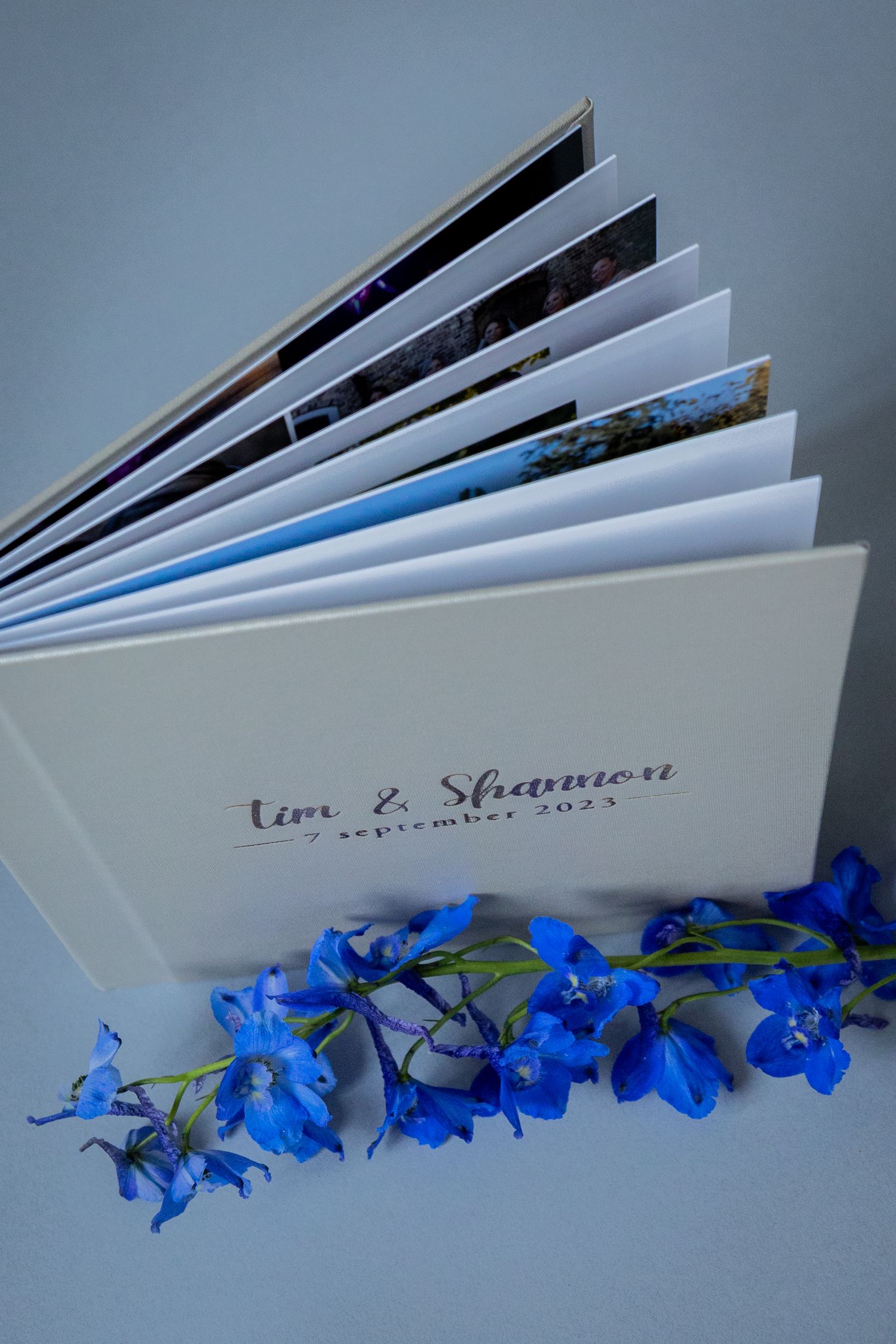 A photo album with bright blue delphinium flowers arranged along its base viewed from multiple angles.