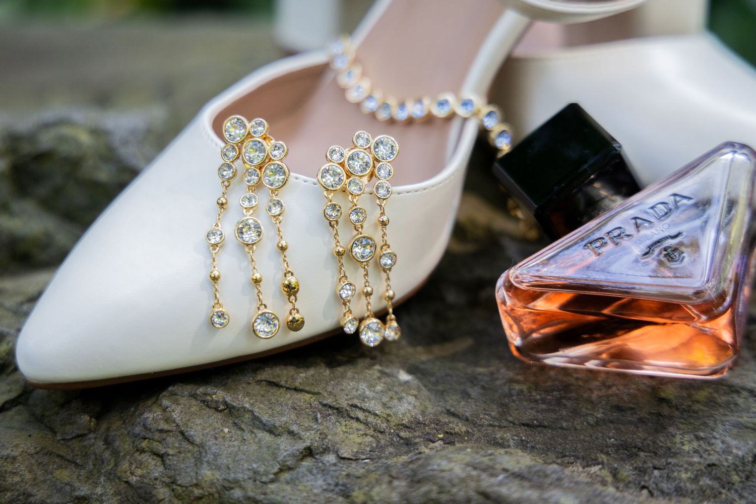 An elegant arrangement of white bridal shoes with crystal embellishments styled with gold jewelry and a perfume bottle.