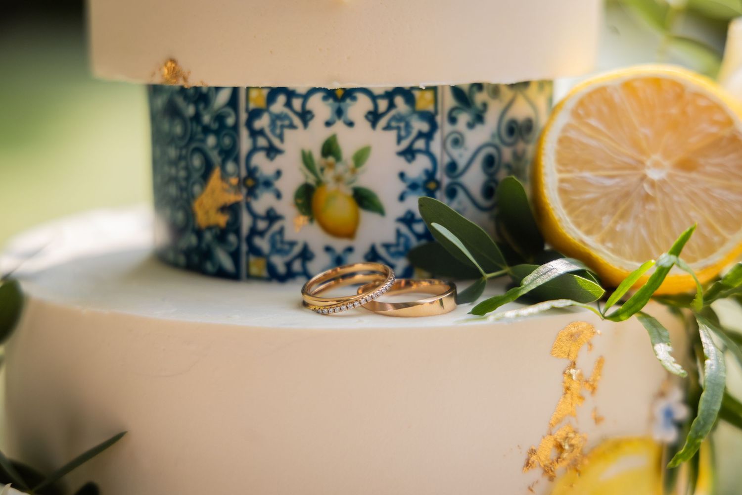 Wedding rings rest beside fresh lemons and a decorative porcelain container with blue floral citrus motif.