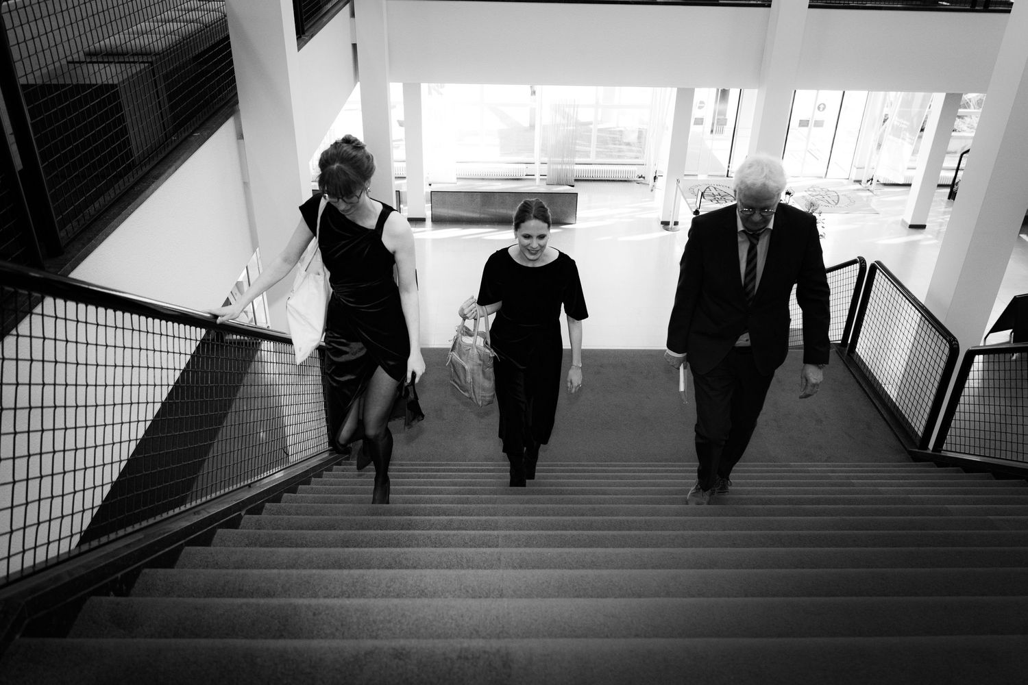 Three people descending a modern staircase in black and white photography.