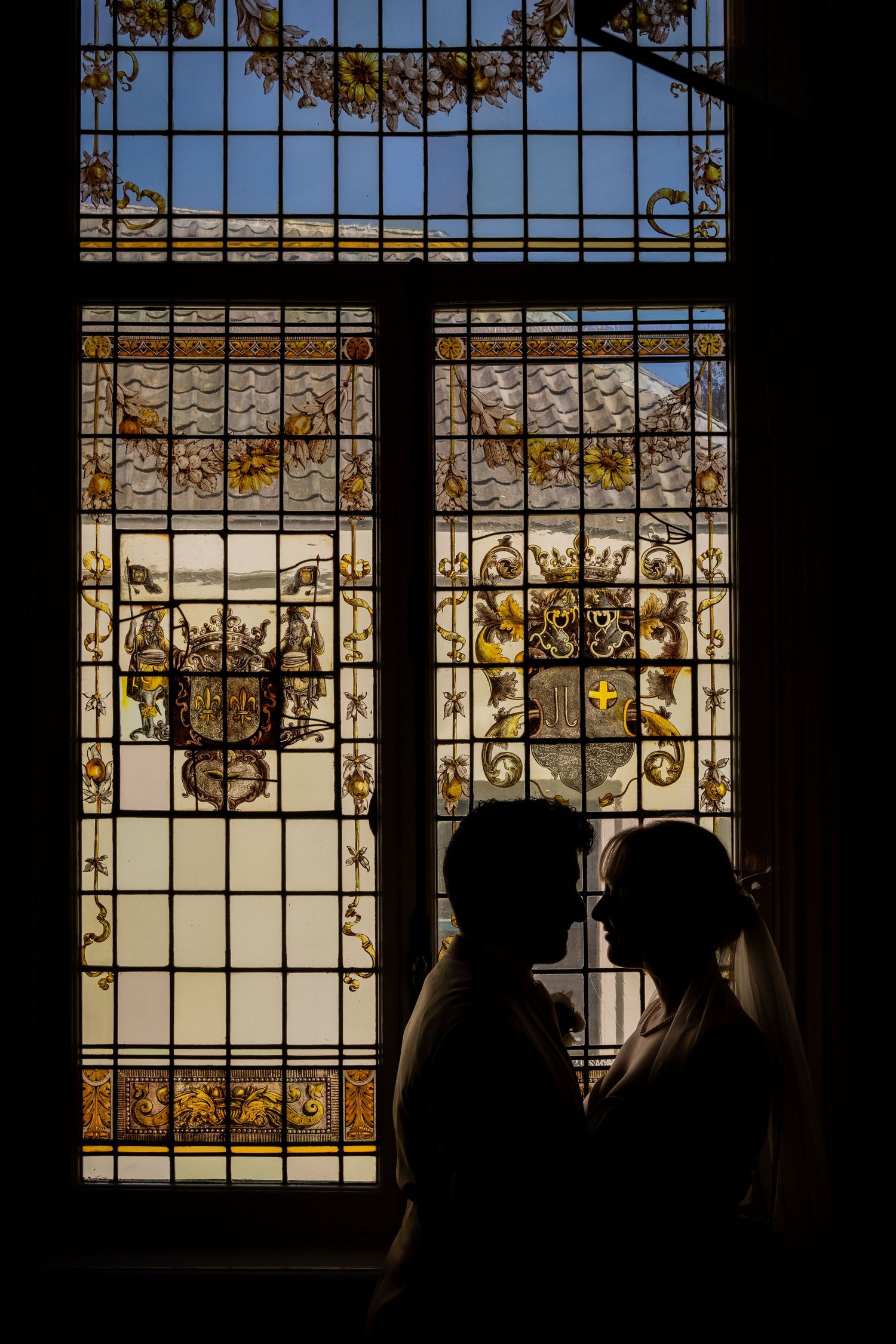 Silhouettes against ornate stained glass windows create artistic wedding photography composition.