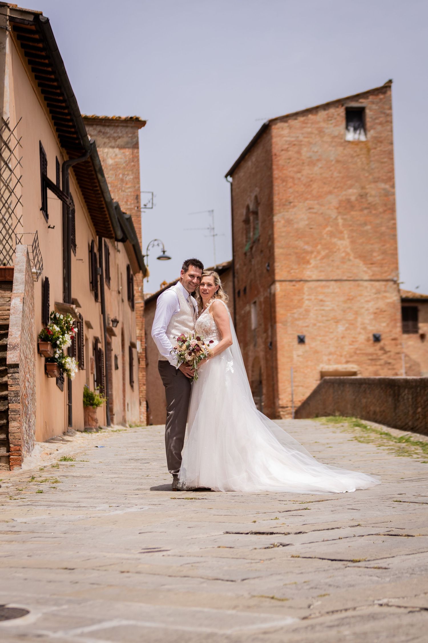 A couple walks together down a charming cobblestone street lined with rustic terracotta buildings in Italy.