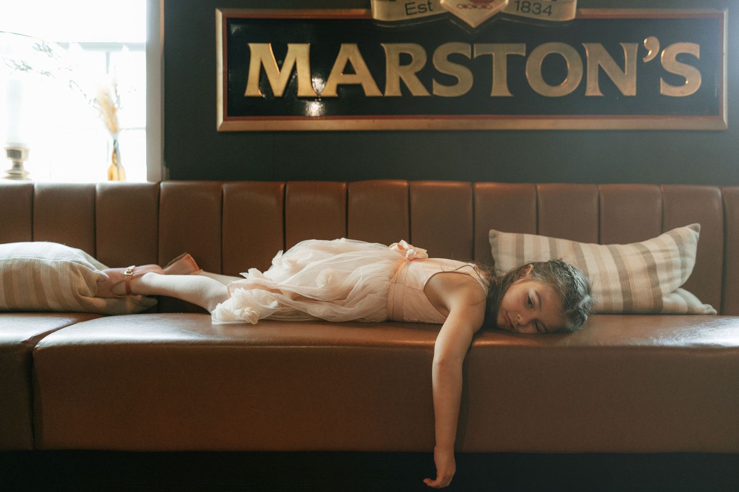 A person lying on a brown leather booth seat beneath a Marston's pub sign.
