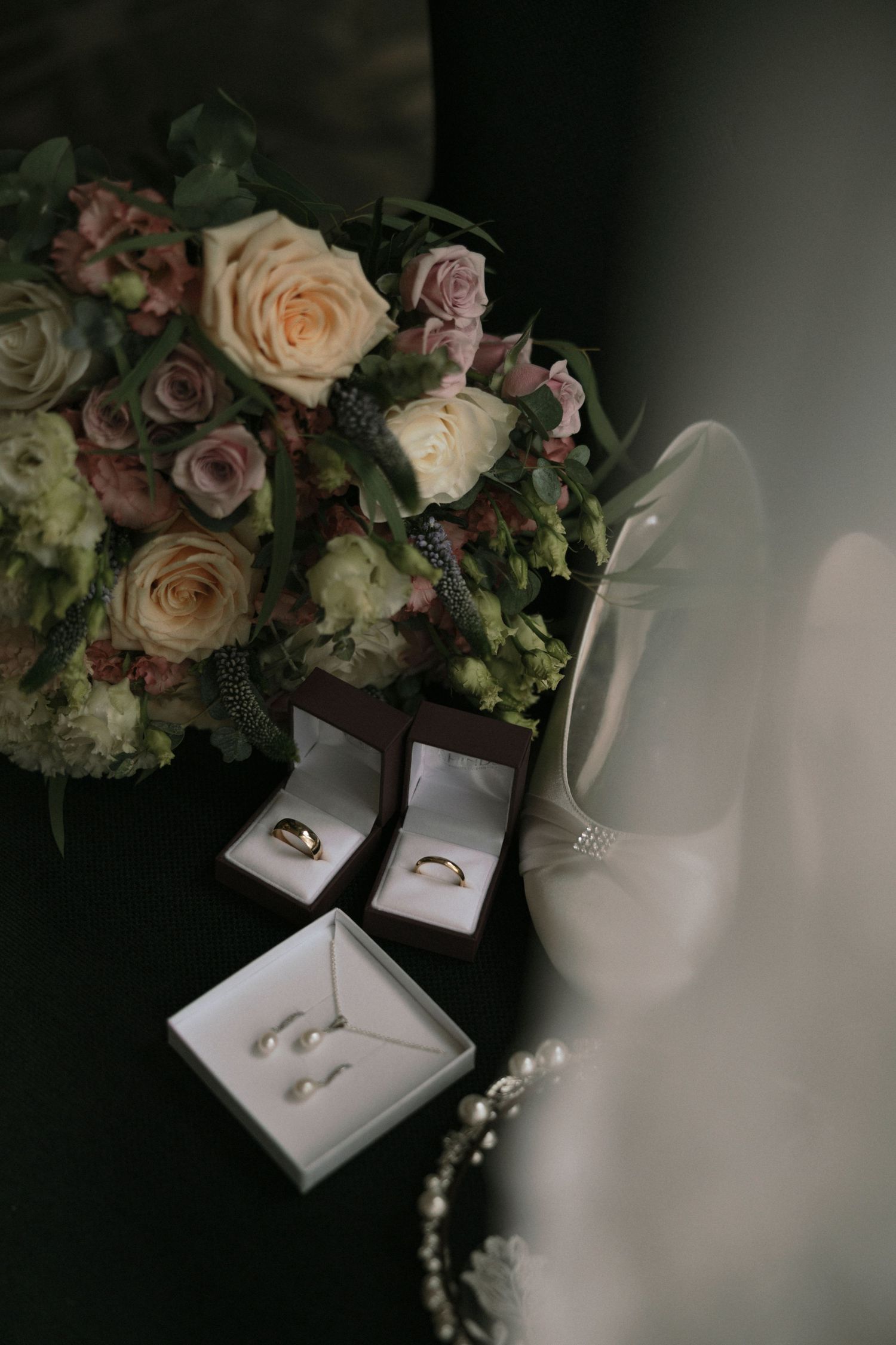 Wedding flat lay with bridal bouquet, gold rings, pearl earrings necklace set, and white heels.