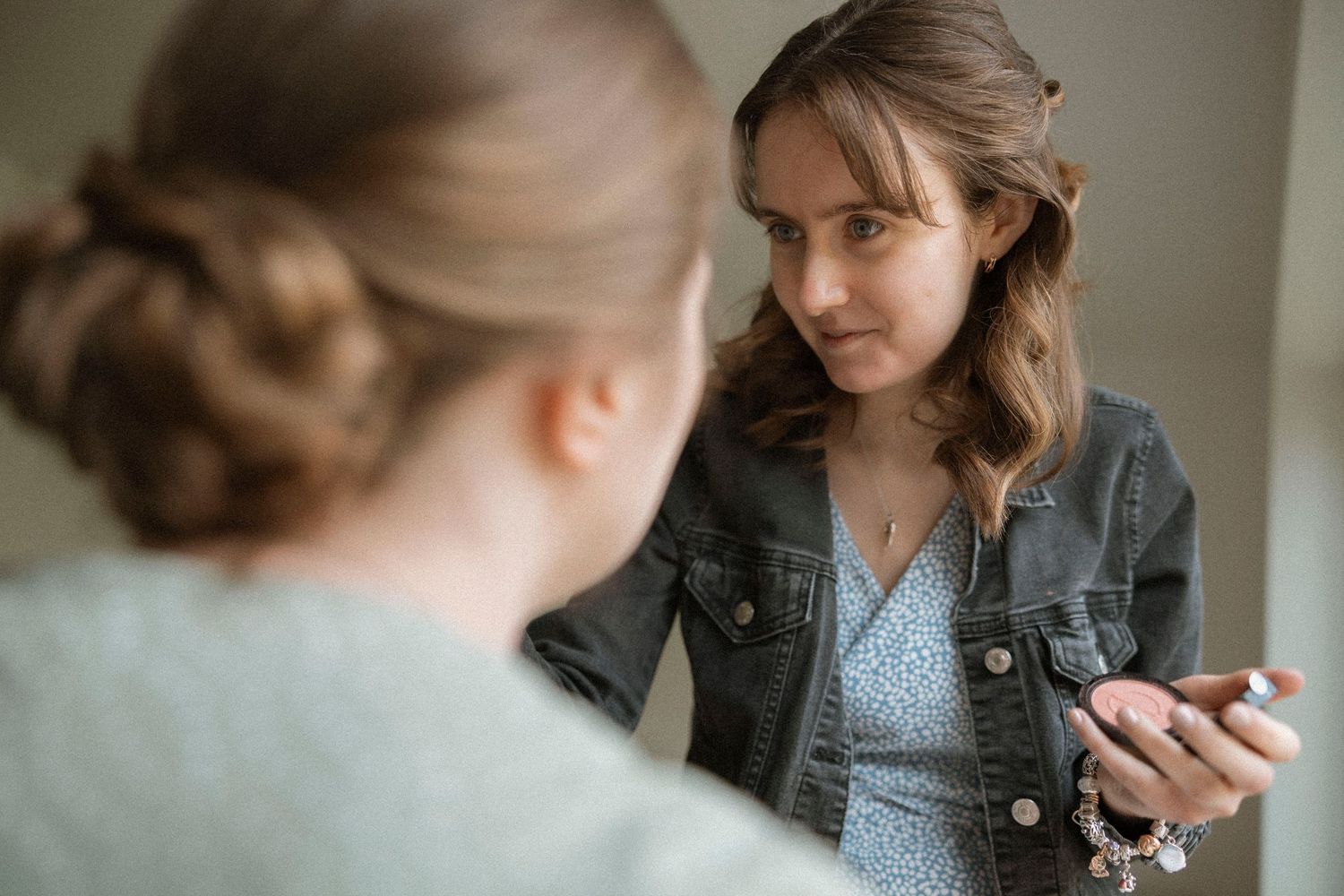 Two young women having a serious conversation, one holding a phone, indoors with soft natural lighting.