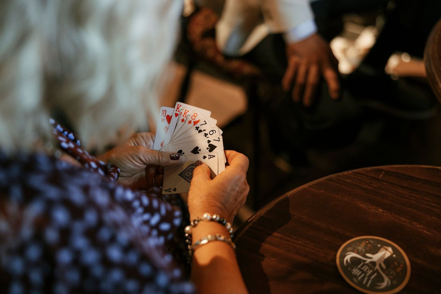 A close-up shot of hands holding playing cards during a poker game at a wooden table.