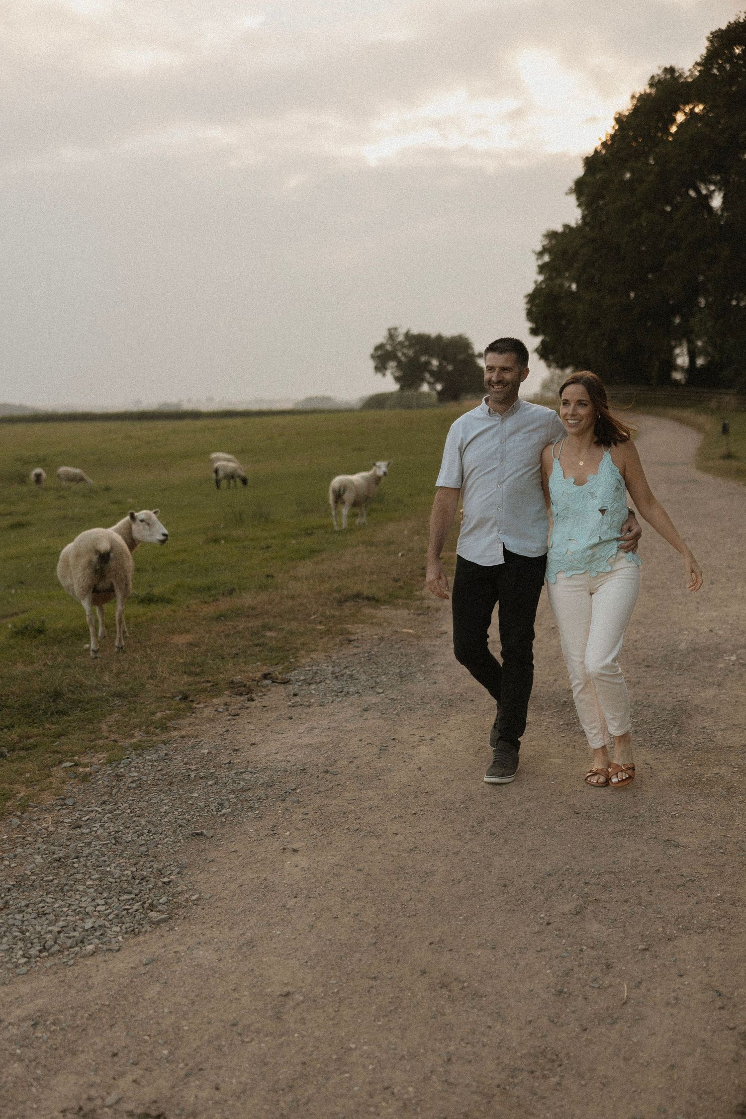 Couple strolling along country path with grazing sheep in pastoral setting.