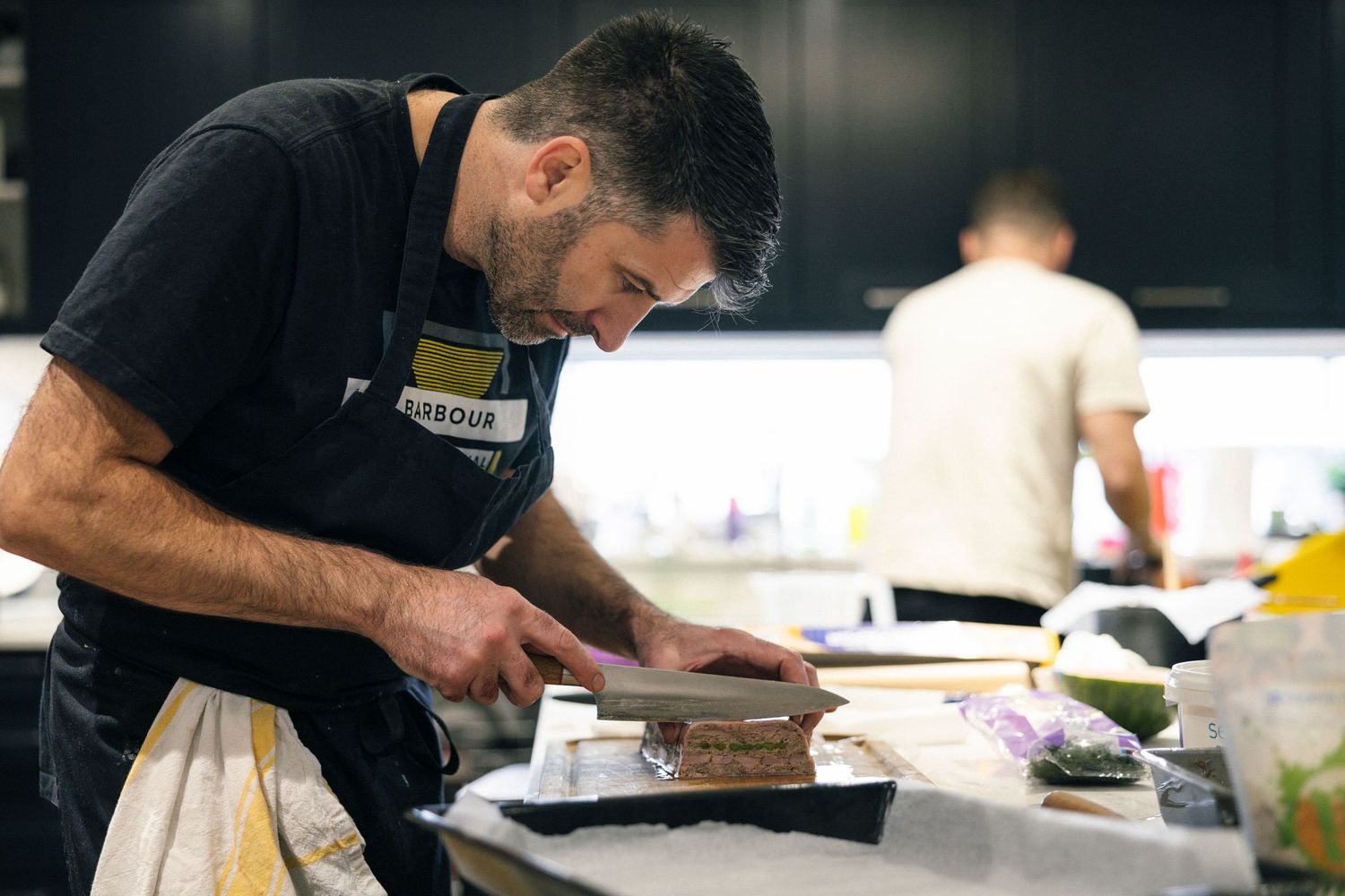 Chef preparing food on a cutting board in a professional kitchen, focused on culinary work.