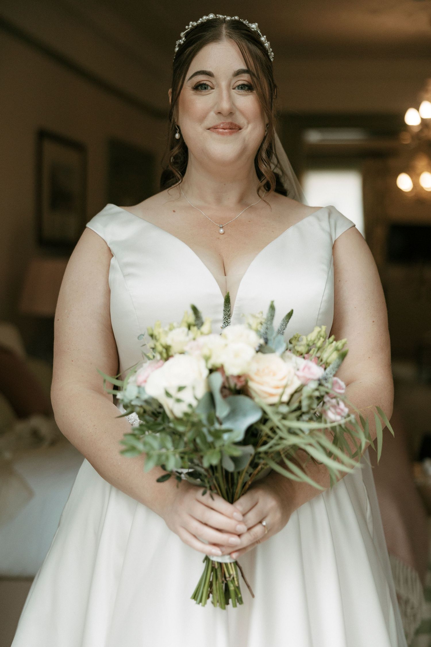 Bride in white ball gown holding pink and white bouquet with greenery, wearing pearl tiara and necklace.