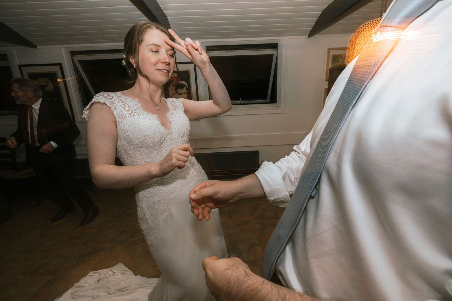 Bride in white lace gown dancing energetically with groom in gray suit at indoor wedding reception.