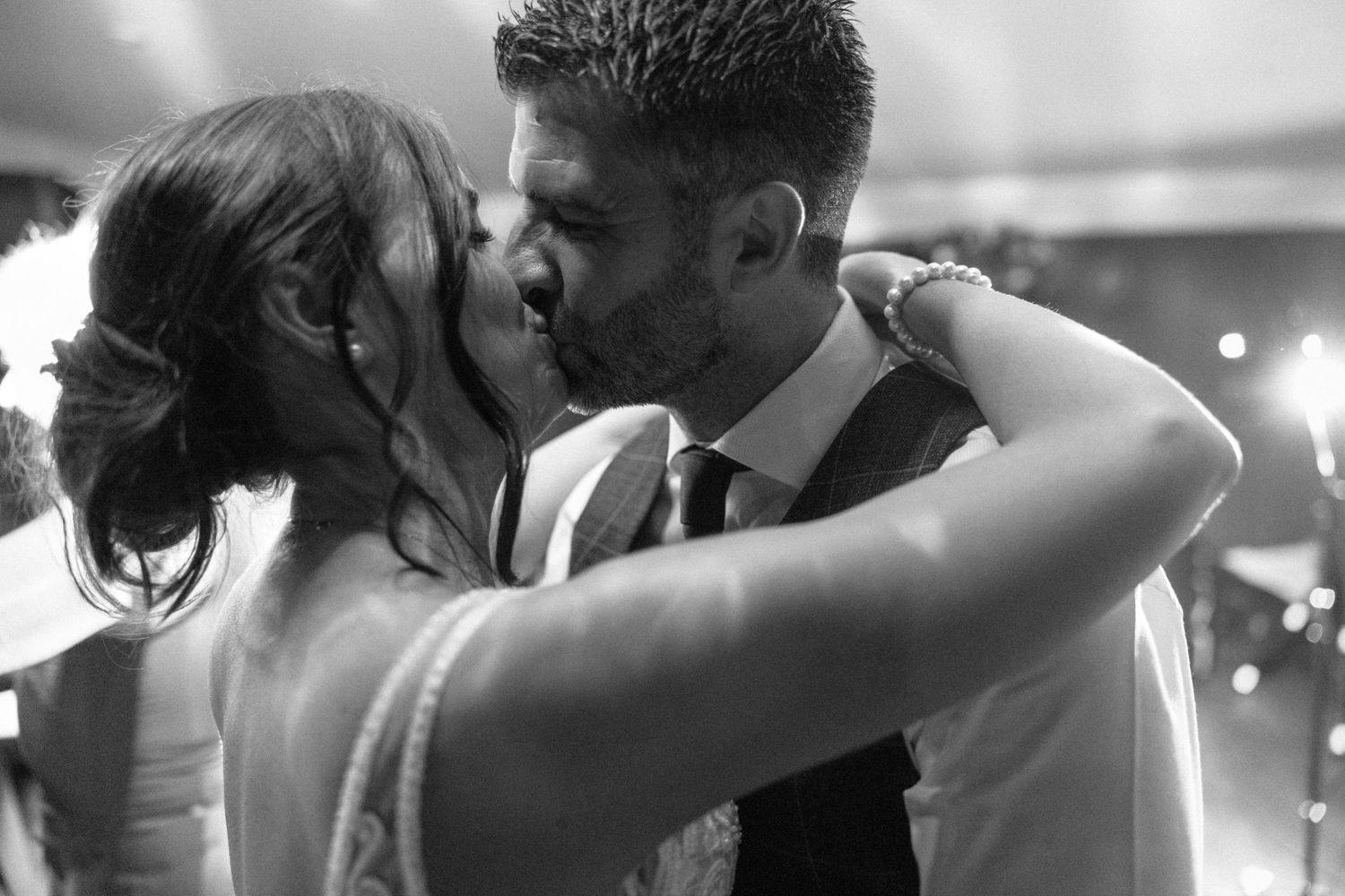 Bride and groom sharing a romantic first kiss at their wedding reception in black and white.