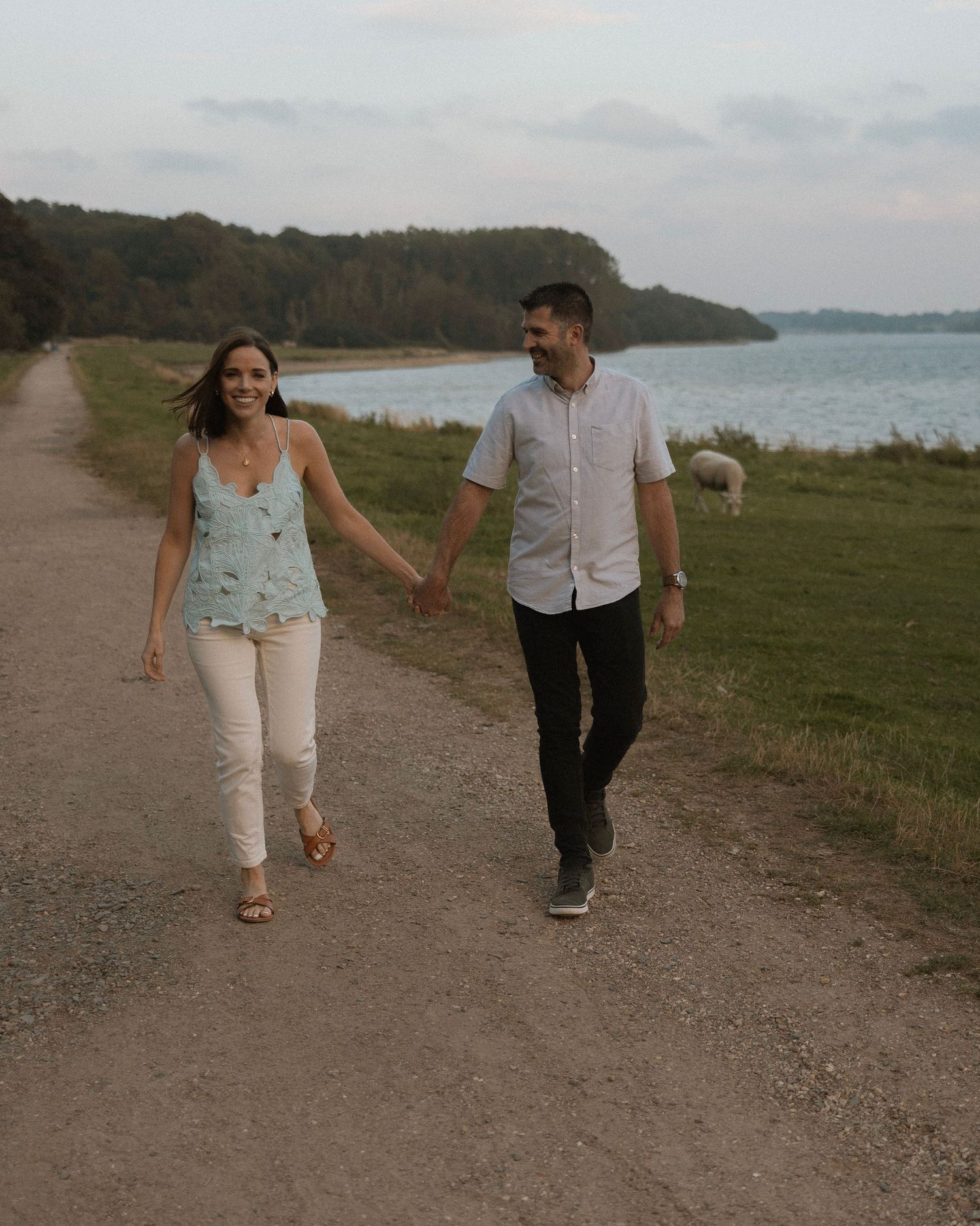 Couple walking hand in hand on coastal path with sheep grazing in background.