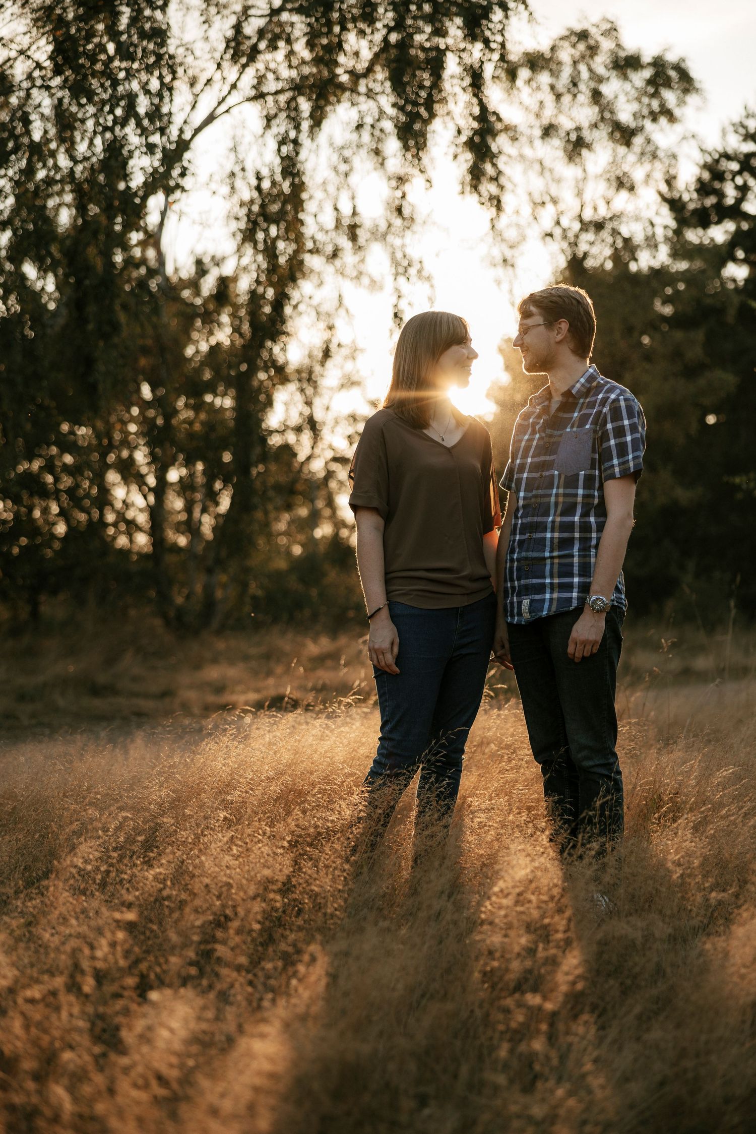 Couple standing face to face in a sunlit meadow during a beautiful golden sunset.