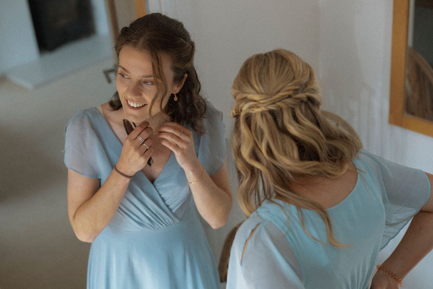 Two bridesmaids in light blue dresses laughing and chatting while getting ready for a wedding ceremony.