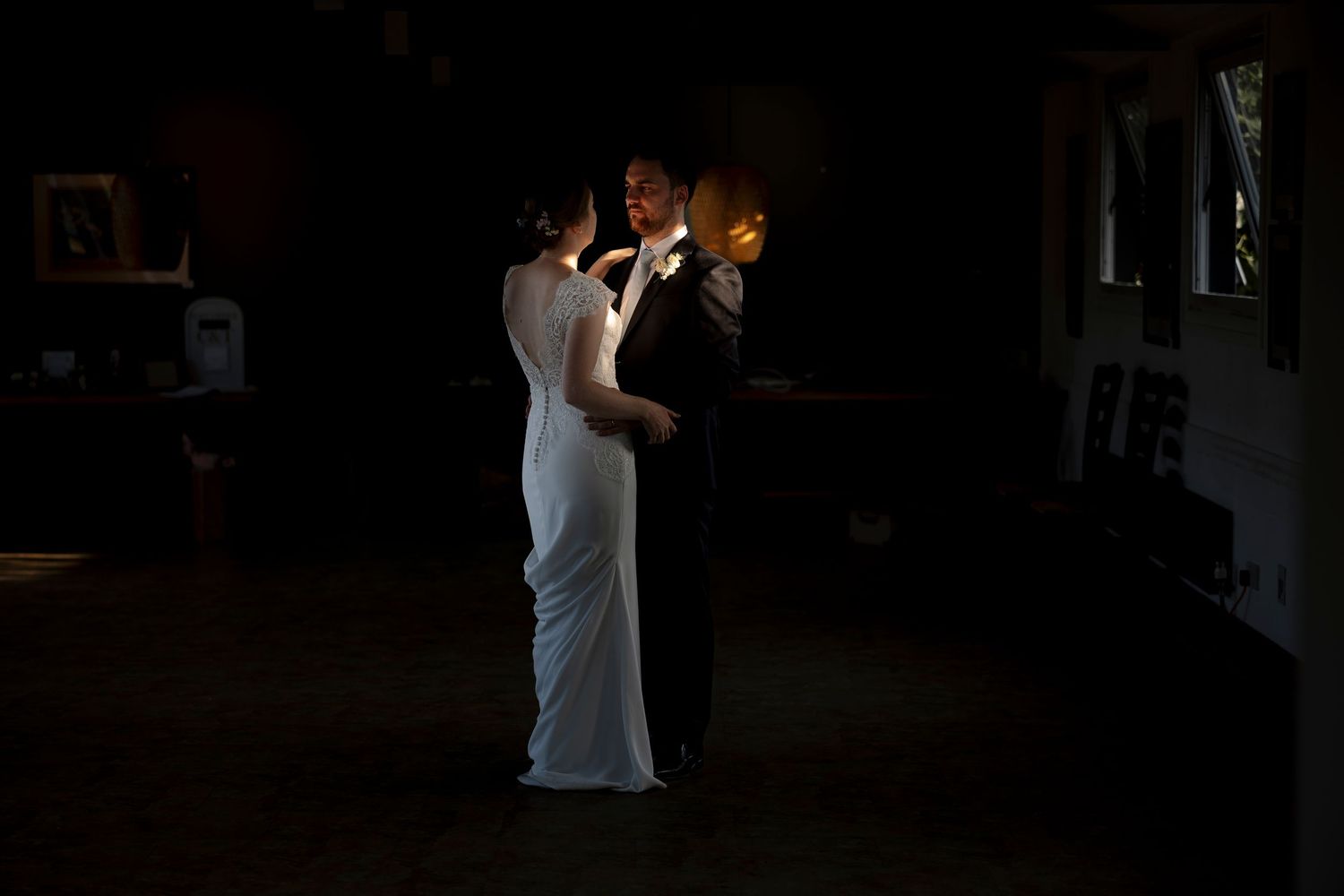 Bride and groom share first dance in dimly lit venue, illuminated by warm candlelight on their wedding day.