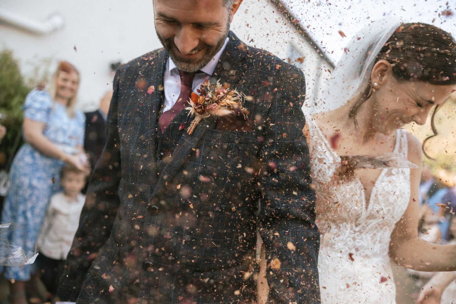 Wedding guests celebrate by throwing confetti at newlyweds in outdoor ceremony as joyful celebration unfolds.