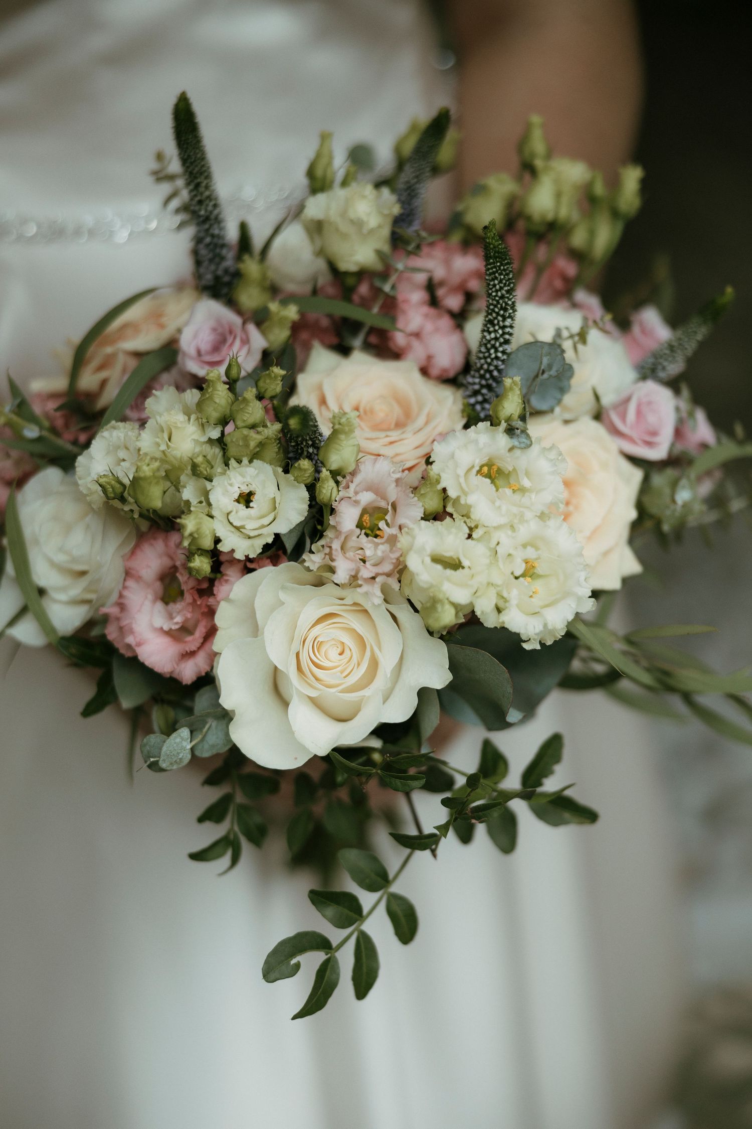 Bride holding elegant bouquet of white and pink roses with eucalyptus greenery on wedding day.