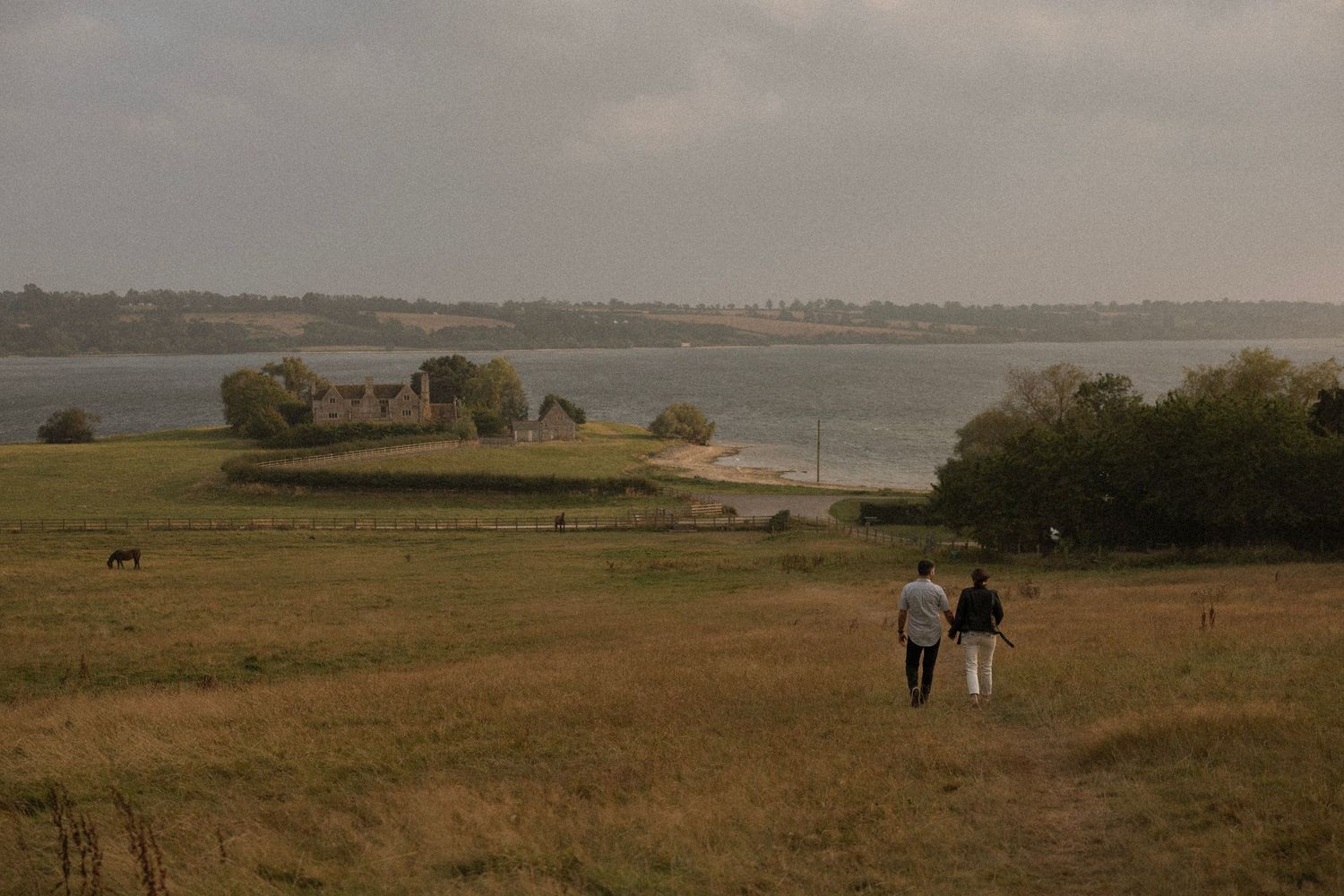 Couple walking through scenic countryside with water view in distance.