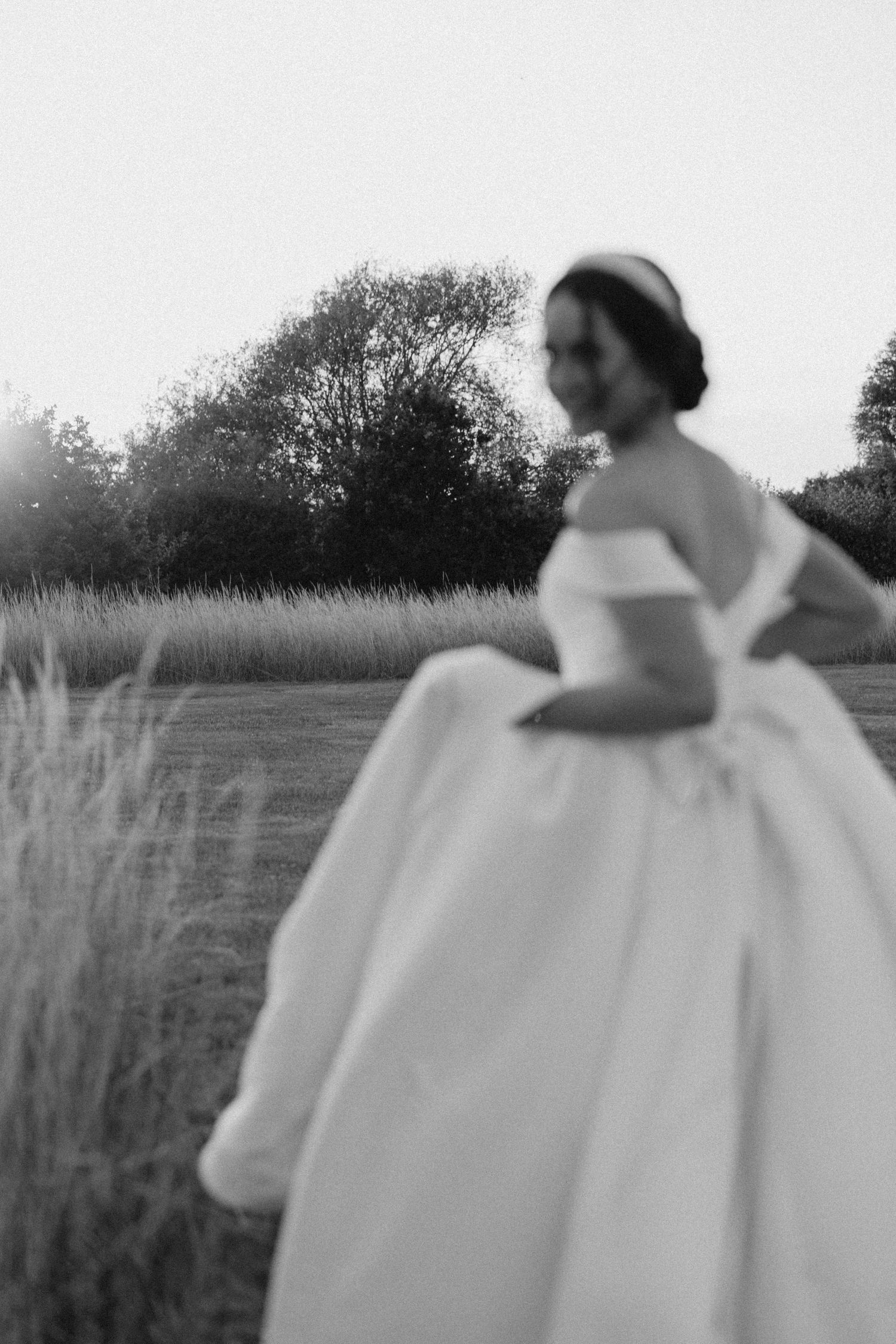 Blurred black and white photo of a bride in an off-shoulder ball gown standing in a field.