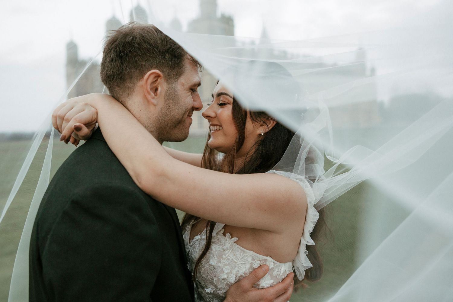 A bride and groom share a romantic moment under a flowing veil at their outdoor wedding ceremony.
