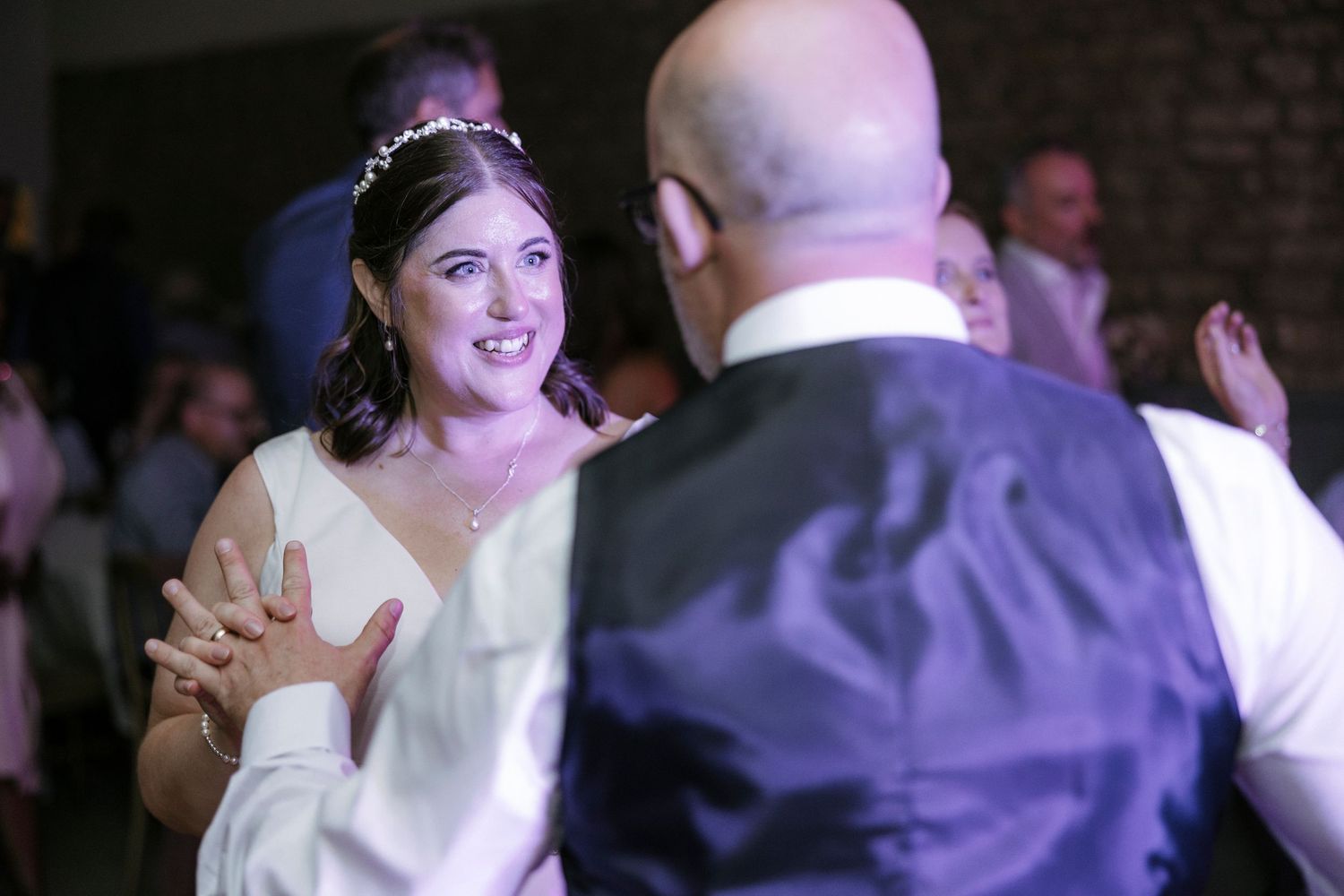 Bride in white dress and floral headpiece sharing first dance with groom at wedding reception.