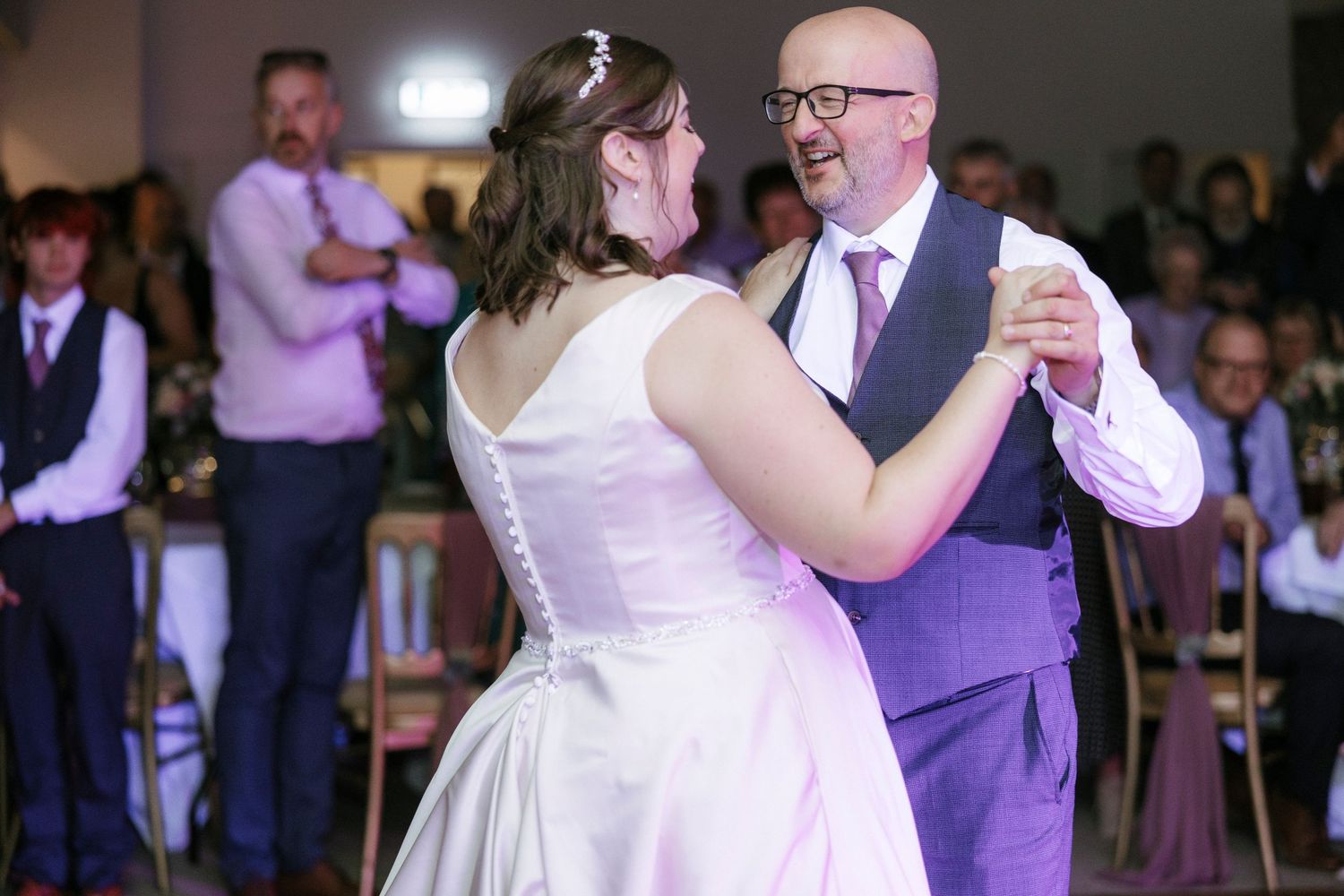 Bride and groom share first dance at wedding reception, smiling joyfully on the dance floor.