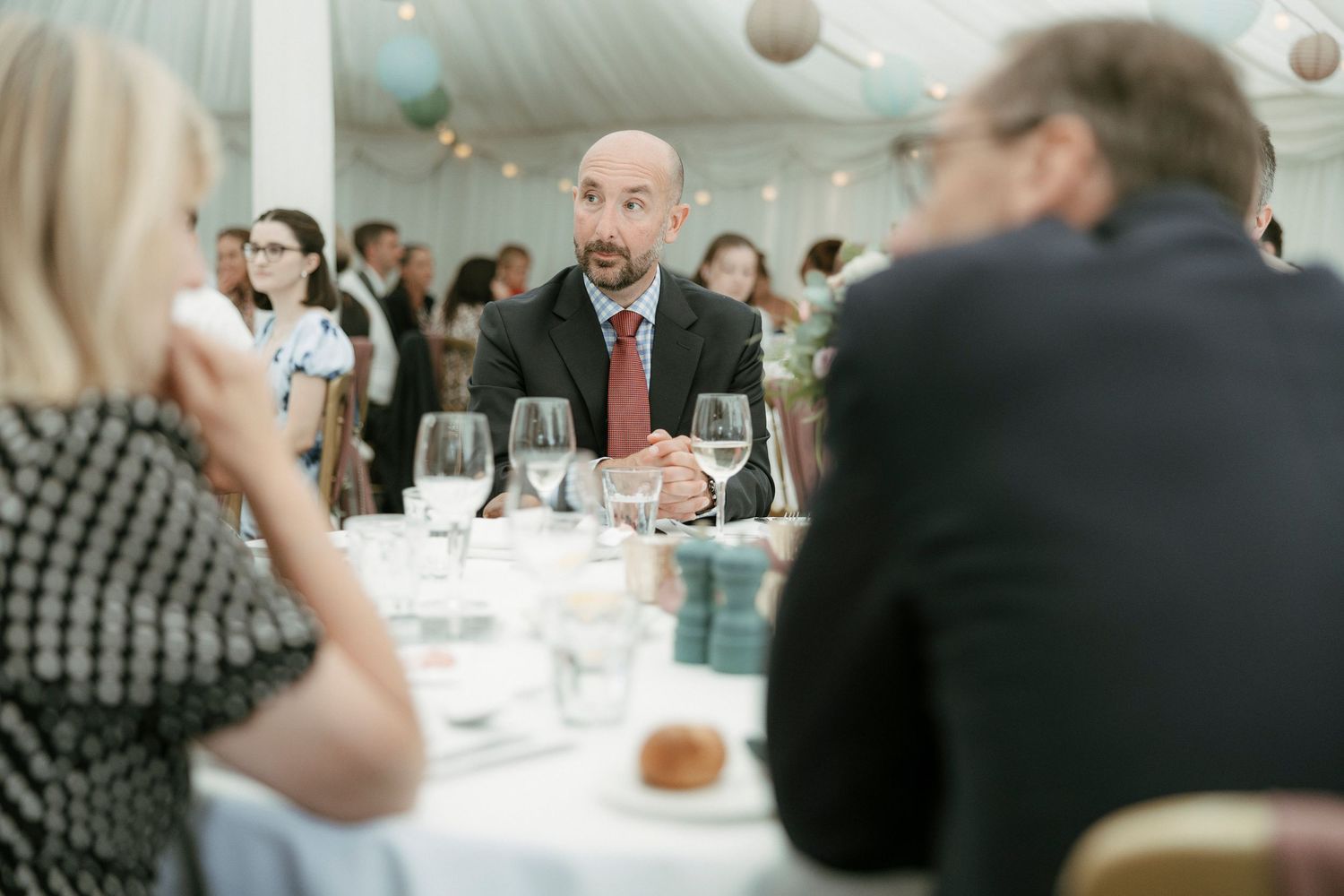 Man in suit engaged in conversation at a formal wedding reception dinner table.