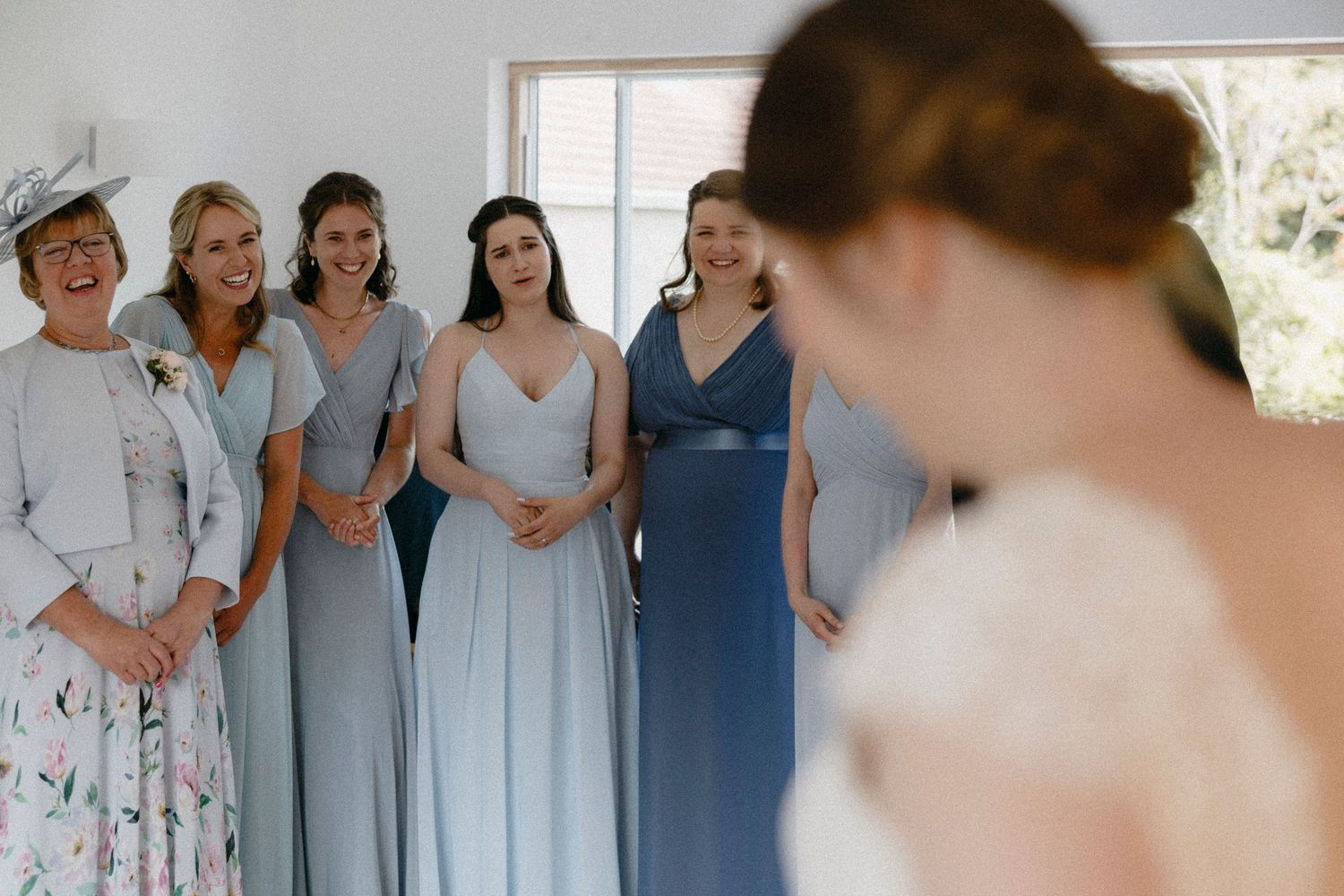 Bridesmaids in blue dresses smiling at bride during wedding getting ready moment indoors.