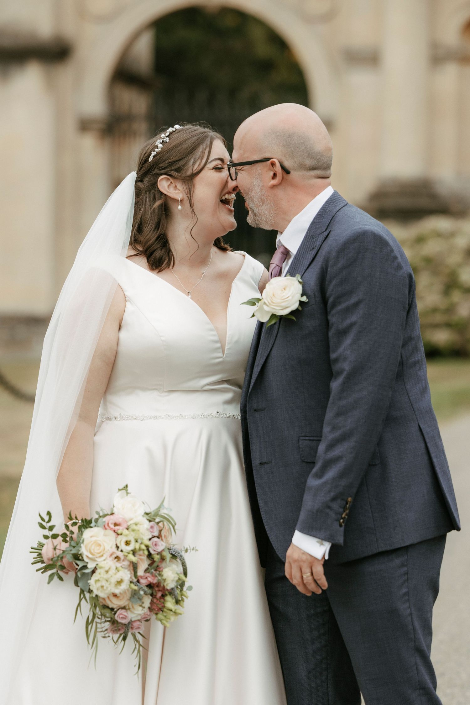 Bride and groom laughing together outdoors holding floral bouquet at wedding.
