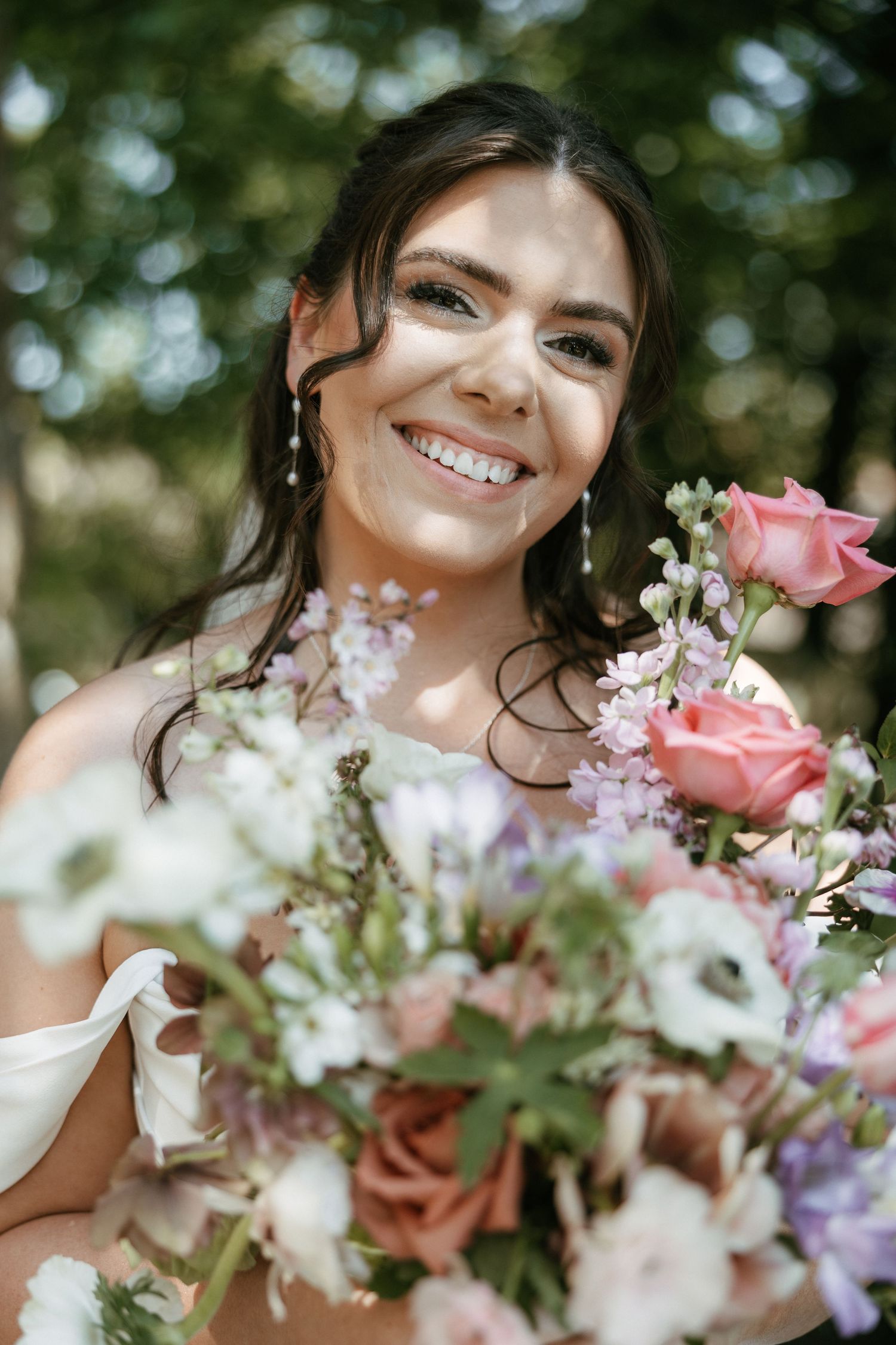 Smiling bride holding a bouquet of pink roses and wildflowers outdoors on her wedding day.