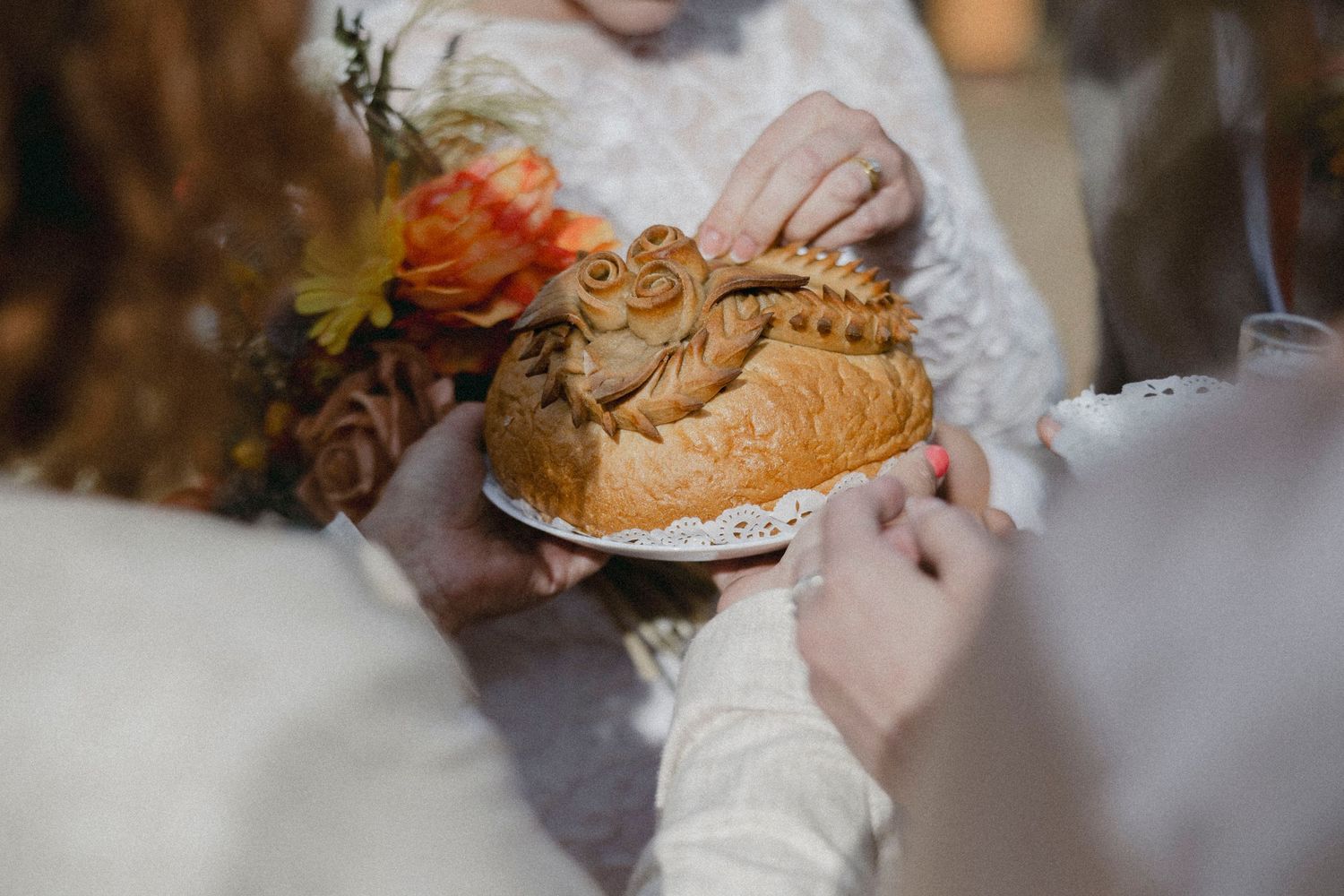 Bride holding decorative braided bread loaf on white plate with orange floral bouquet at wedding ceremony.