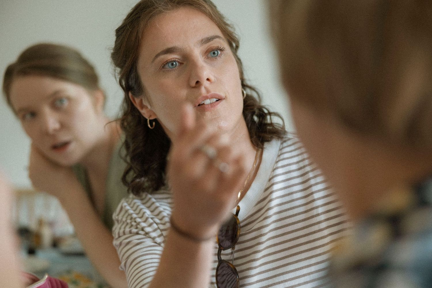 Two women engaged in conversation, one gesturing with her hand while wearing a striped shirt and bracelet.