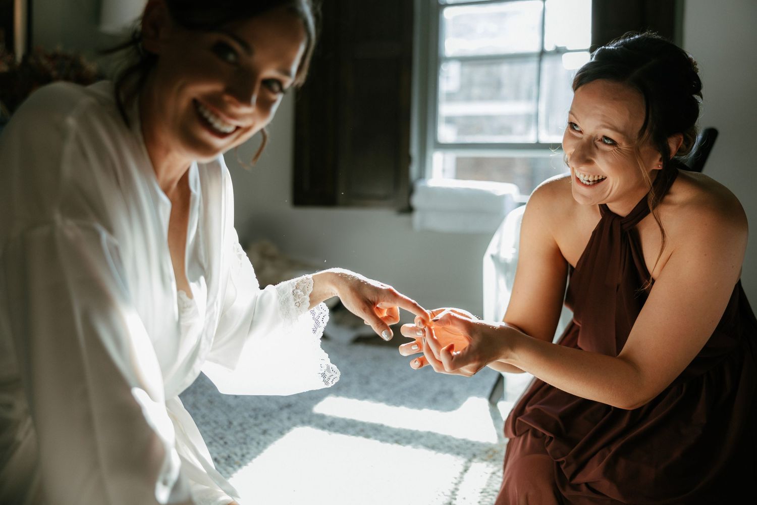 Two people share a joyful moment while getting ready in a sun-filled room.