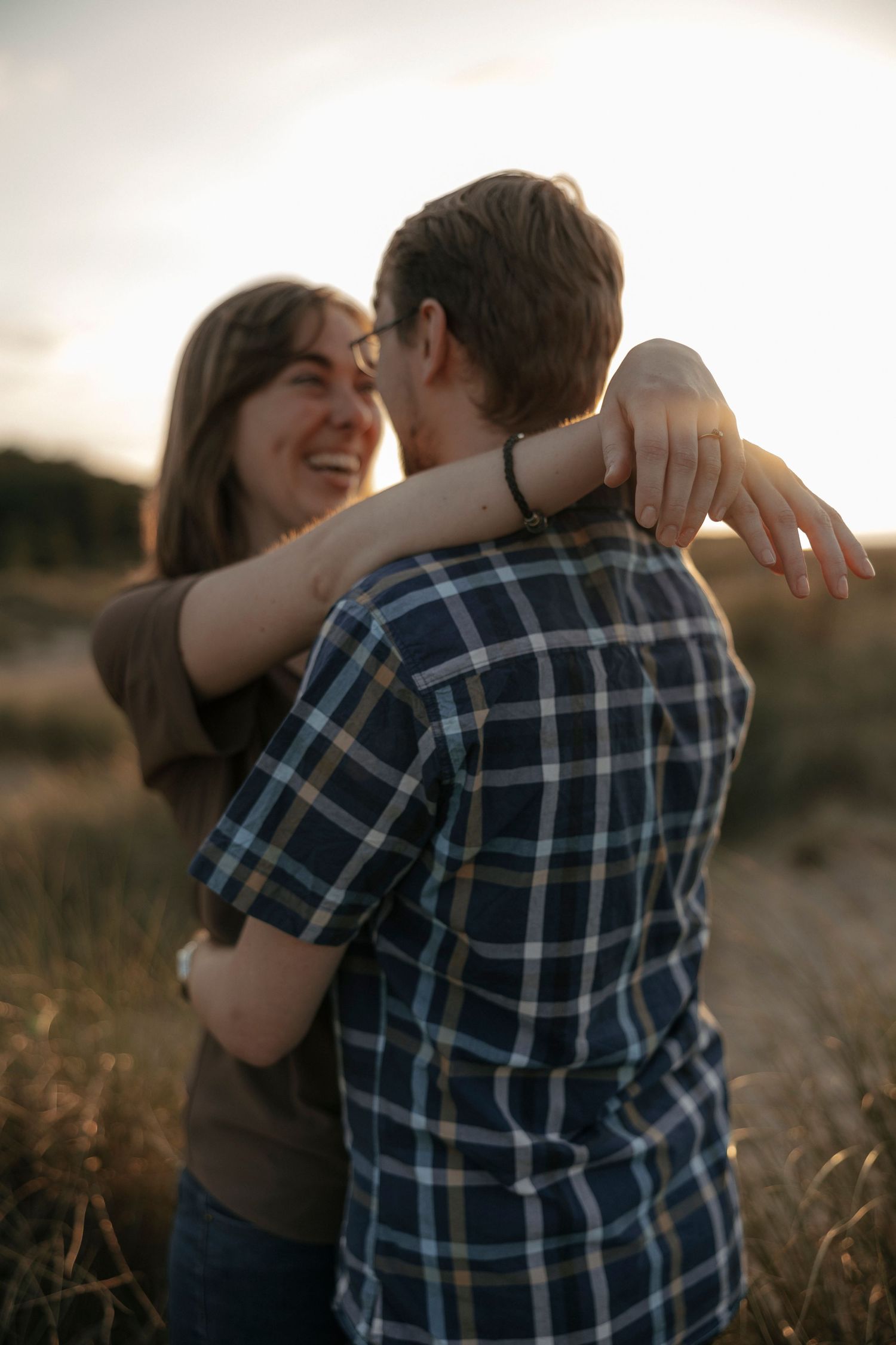 A joyful couple embracing and laughing together in a golden field during a beautiful sunset.