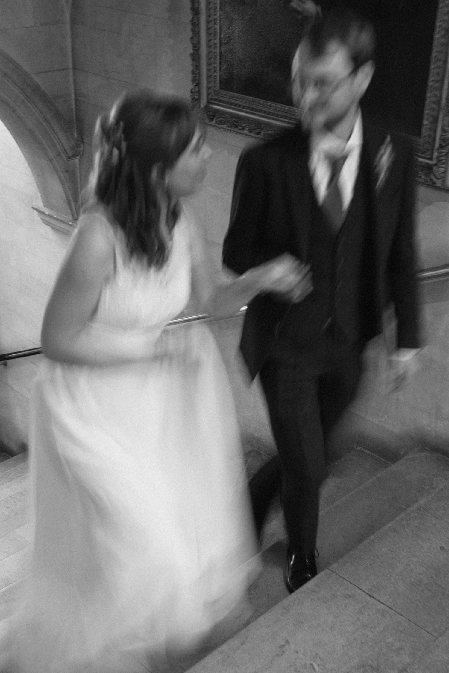 Black and white blurred motion photo of bride and groom walking up stone stairs together on their wedding day.