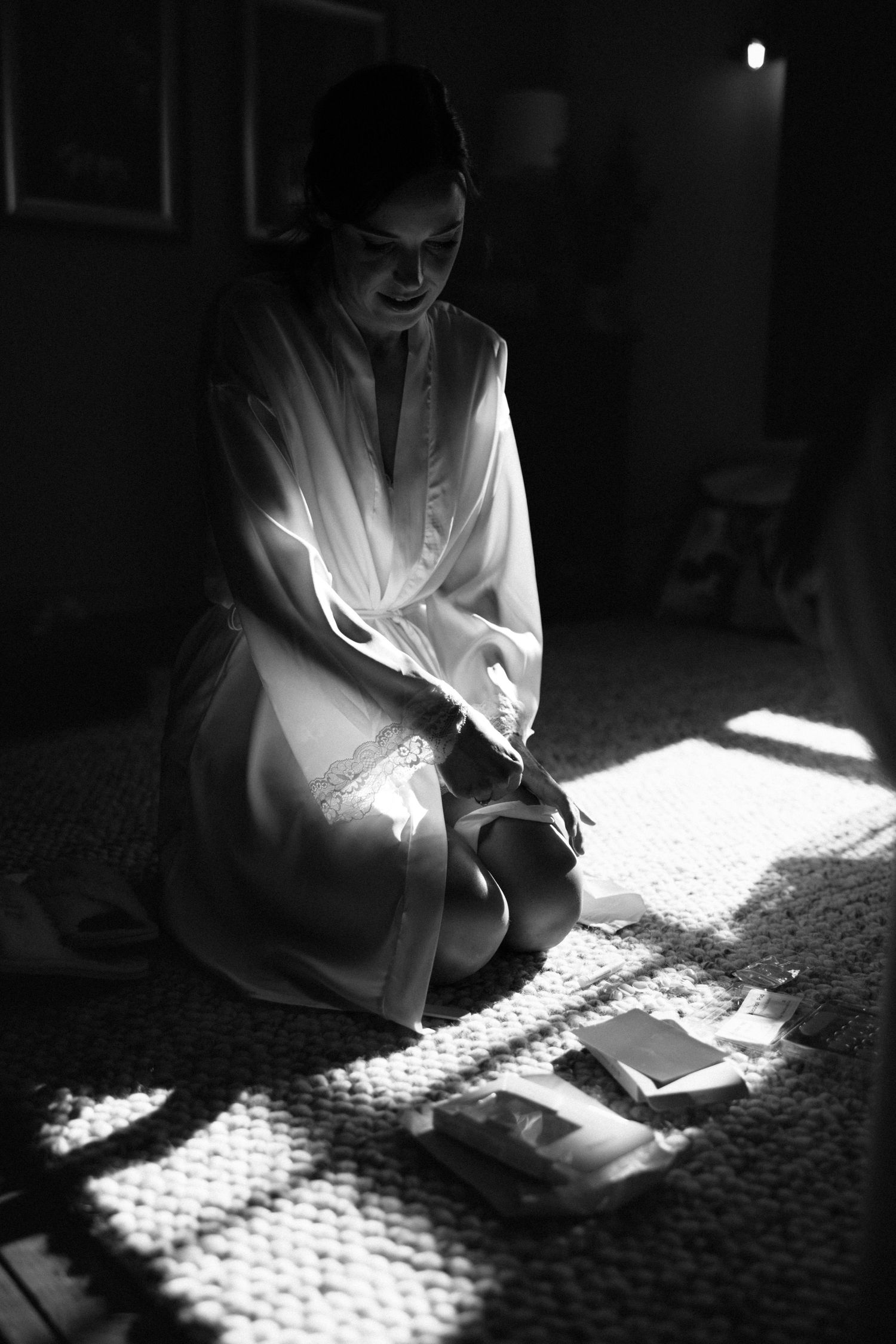 Dramatic black and white photograph of someone in white robe sitting on textured carpet with sunlight creating shadow patterns.